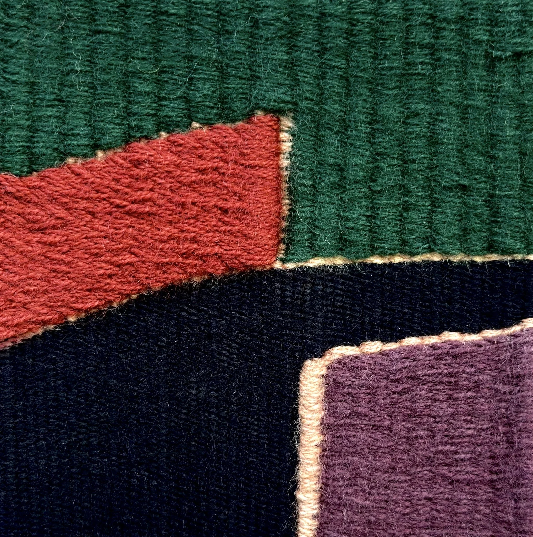 Gros plan d'une partie d'un tapis ou d'un tissu en laine de couleur verte, rouge, noire, blanc et violet, montrant des détails de la texture et des fibres.