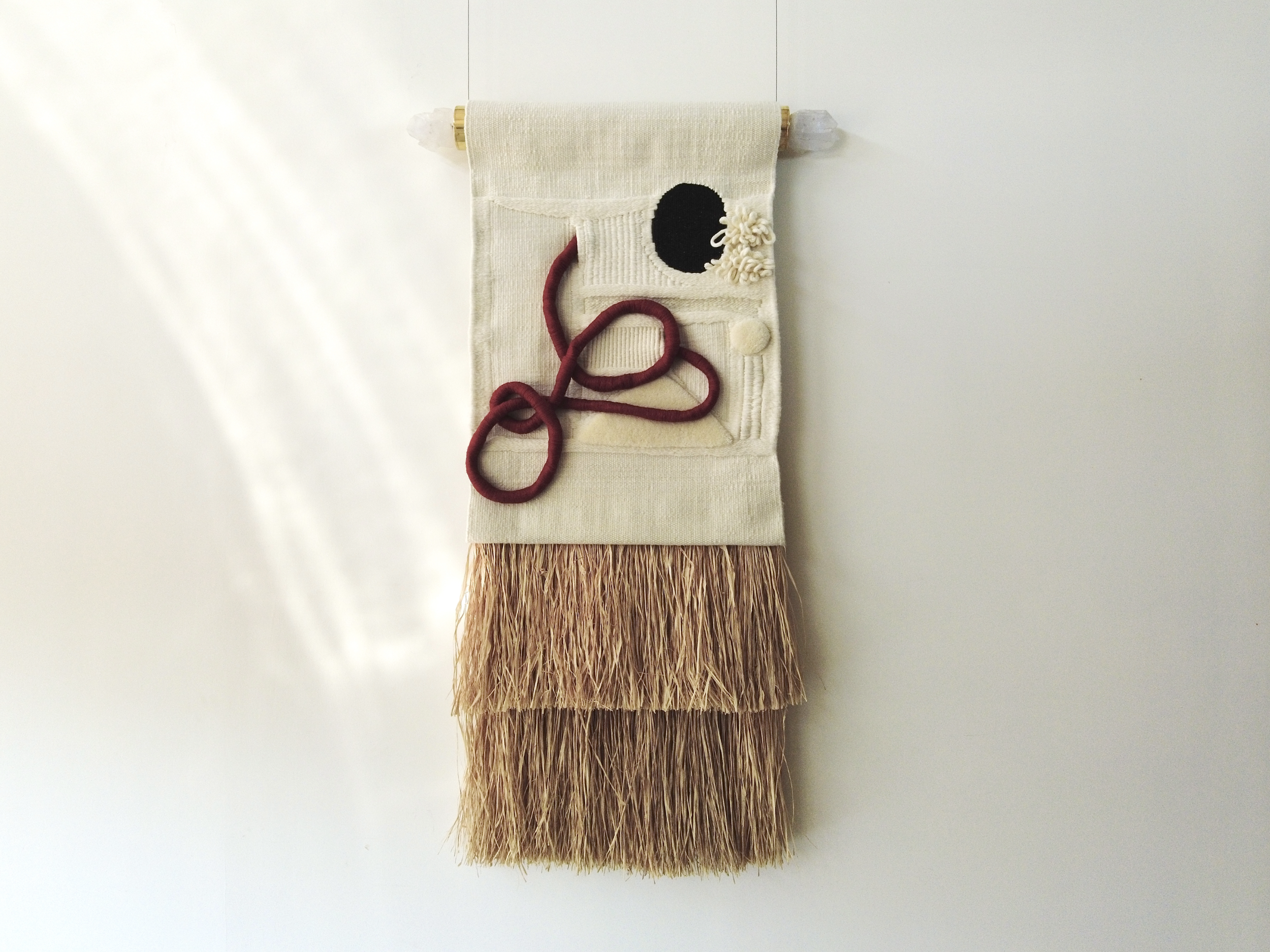 Balai à porte-curieuse en tissu beige avec décoration en forme de cercle noir et textured, suspendu à un mur blanc.