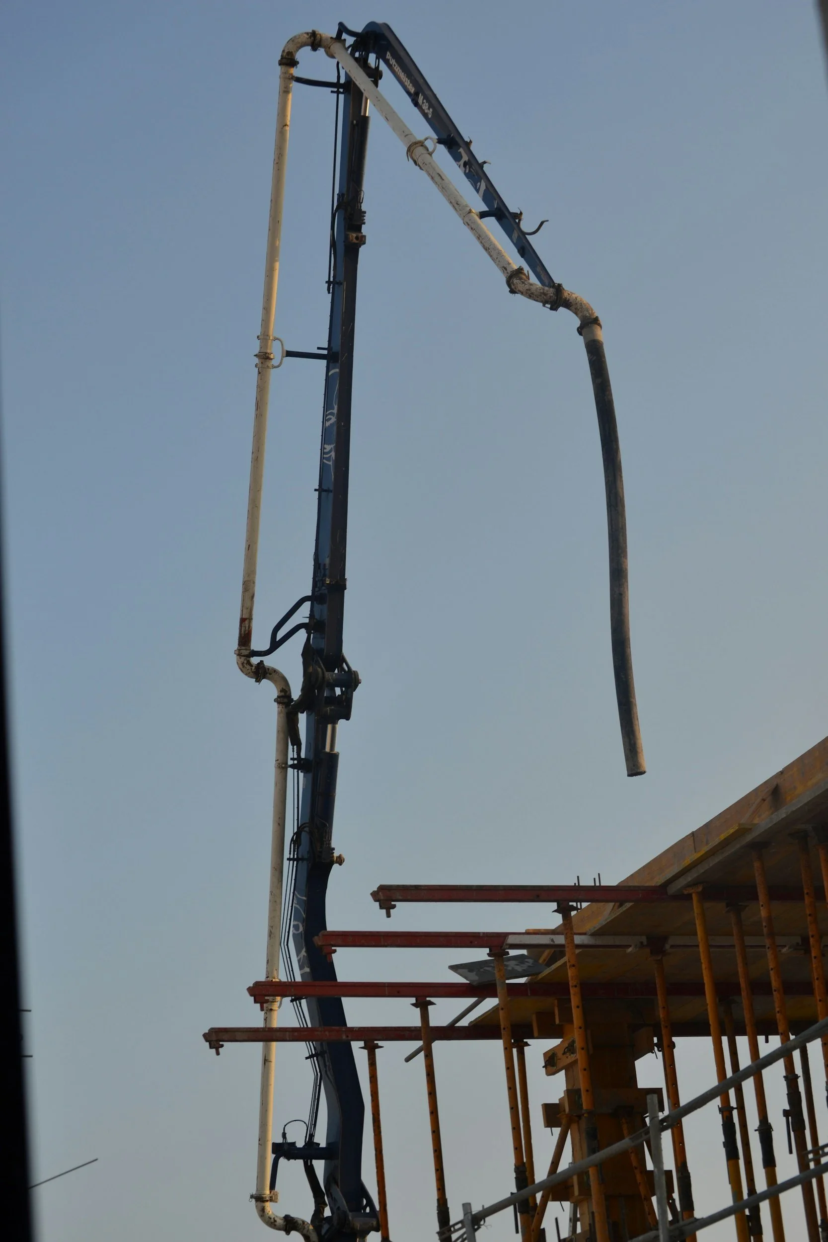 Construction site with a concrete pumping hose and scaffolding against a clear sky.
