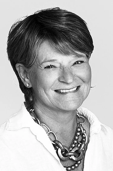 Black and white photo of a smiling woman with short hair, wearing a white shirt and layered necklaces.