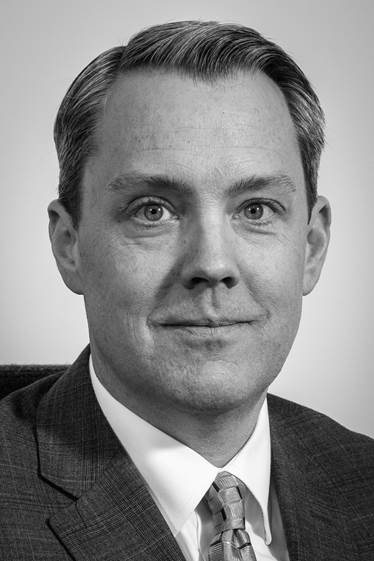 Black and white portrait of a man in a suit with a tie, smiling slightly, with neatly combed hair.
