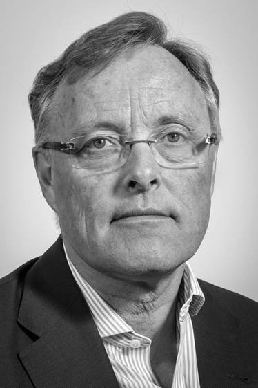 Black and white portrait of a middle-aged man with glasses, wearing a suit and striped shirt, looking serious.