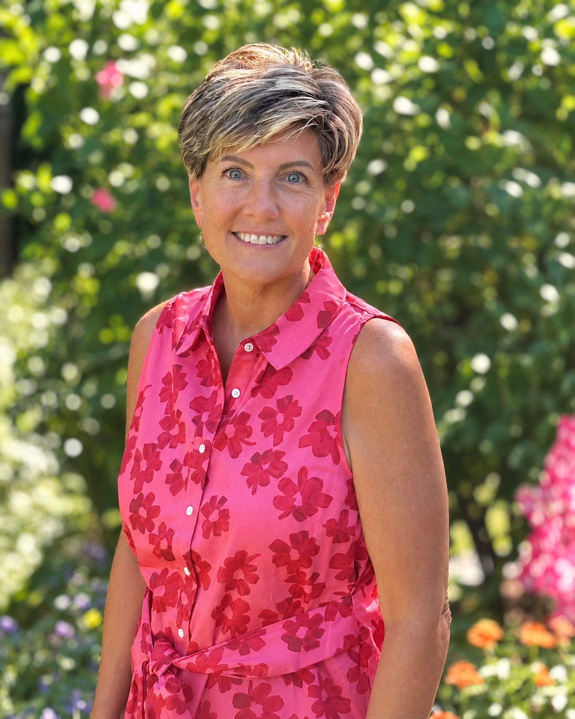 Pam of Redesigning Rooms smiling with short hair wearing a pink floral sleeveless dress outdoors in a garden.