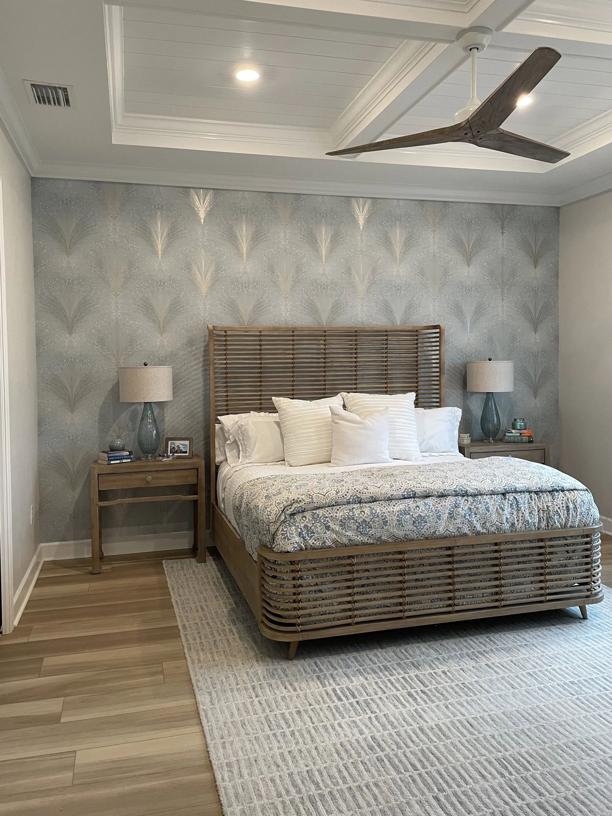 Bedroom featuring subtle blue botanical accent wallpaper behind a woven wood bed, with matching nightstands and lamps.