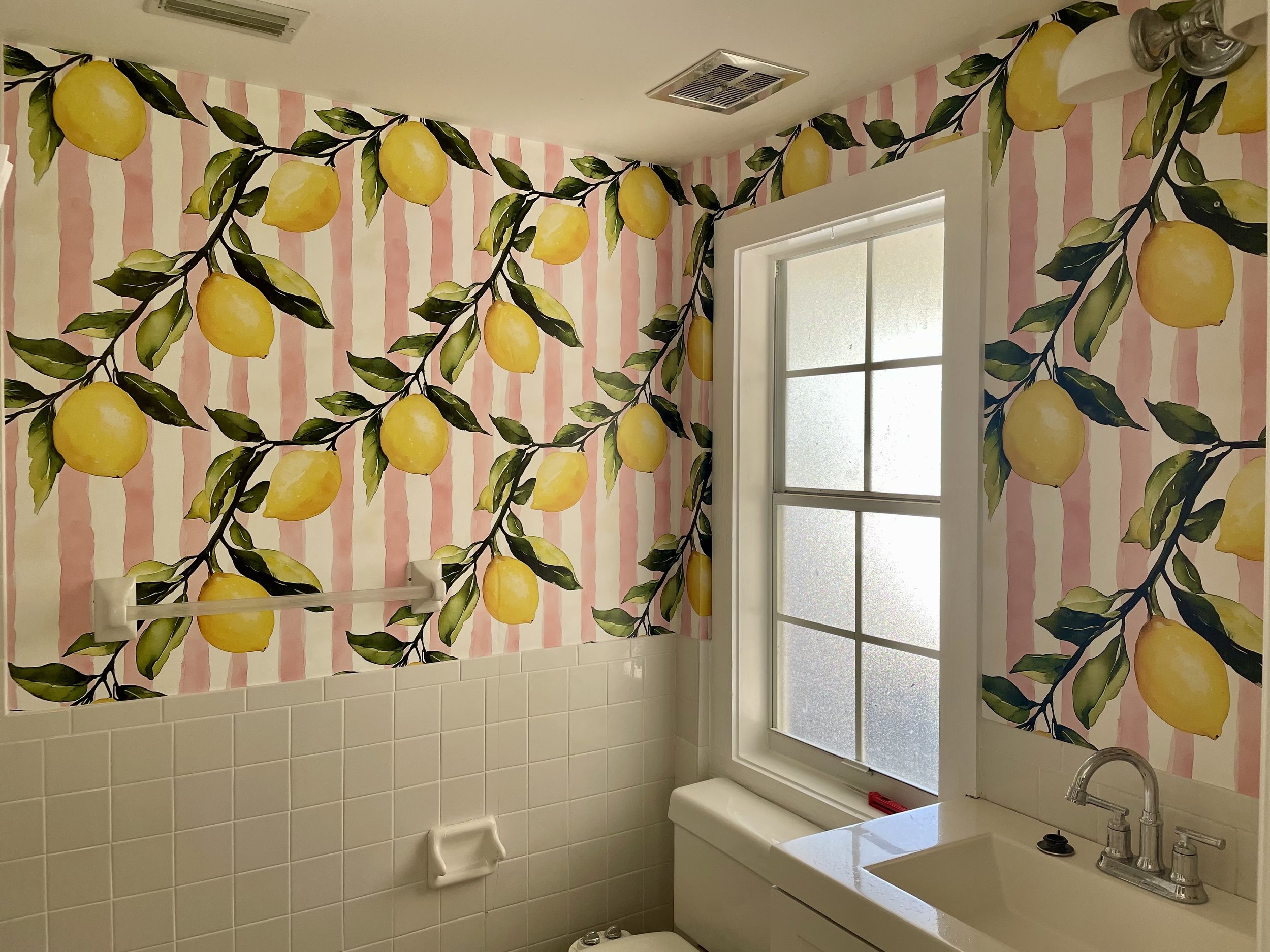 Bathroom with colorful lemon-pattern wallpaper on pink and white stripes, tiled walls, and a bathtub.