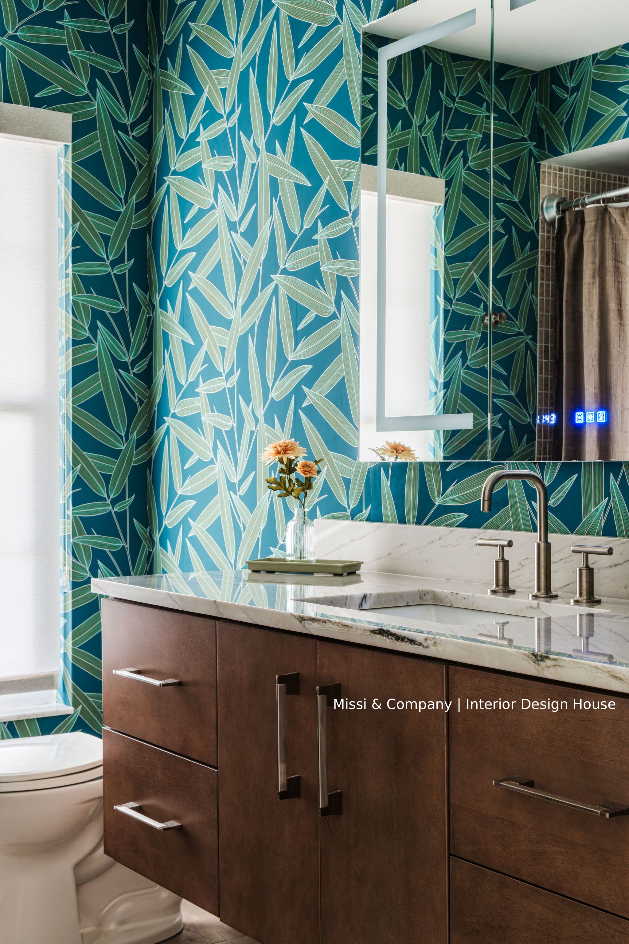 Modern bathroom vanity with dark wood cabinets, marble countertop, wall-mounted faucets, large mirror, and teal bamboo leaf wallpaper