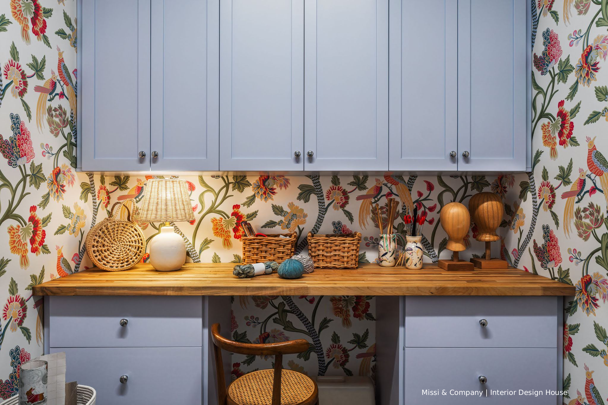 Colorful floral and bird wallpaper in a craft room with light blue cabinets, wood countertop, and sewing supplies.