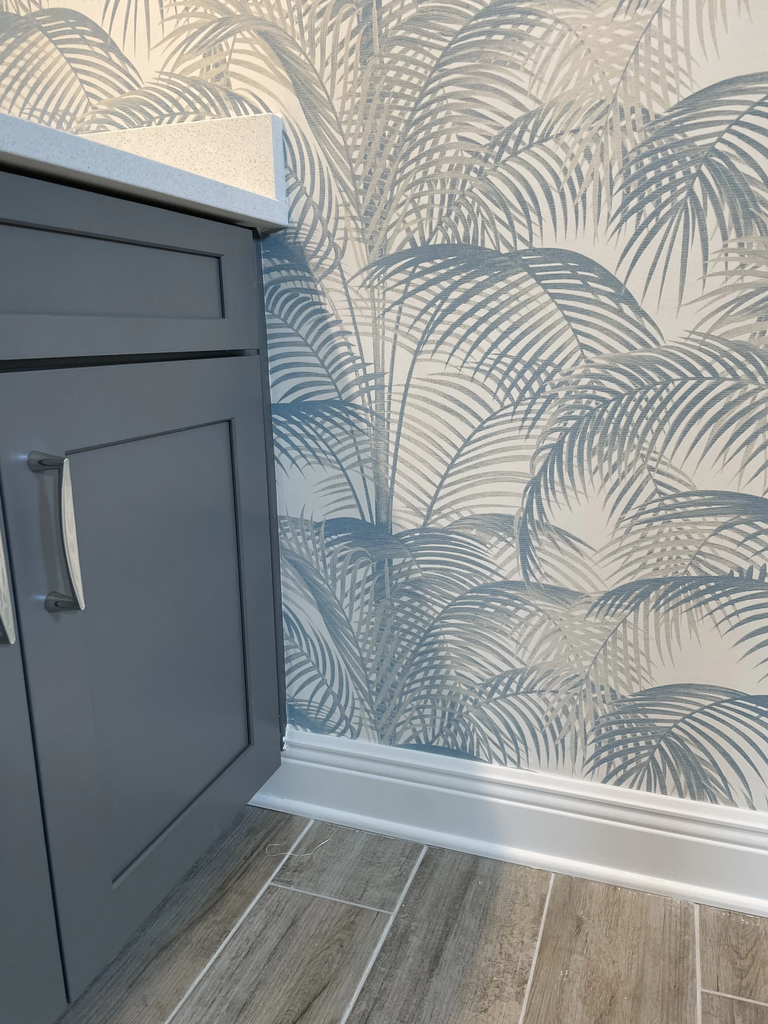 Gray interior door beside blue palm-leaf wallpaper, white baseboard, and wood-look tile flooring