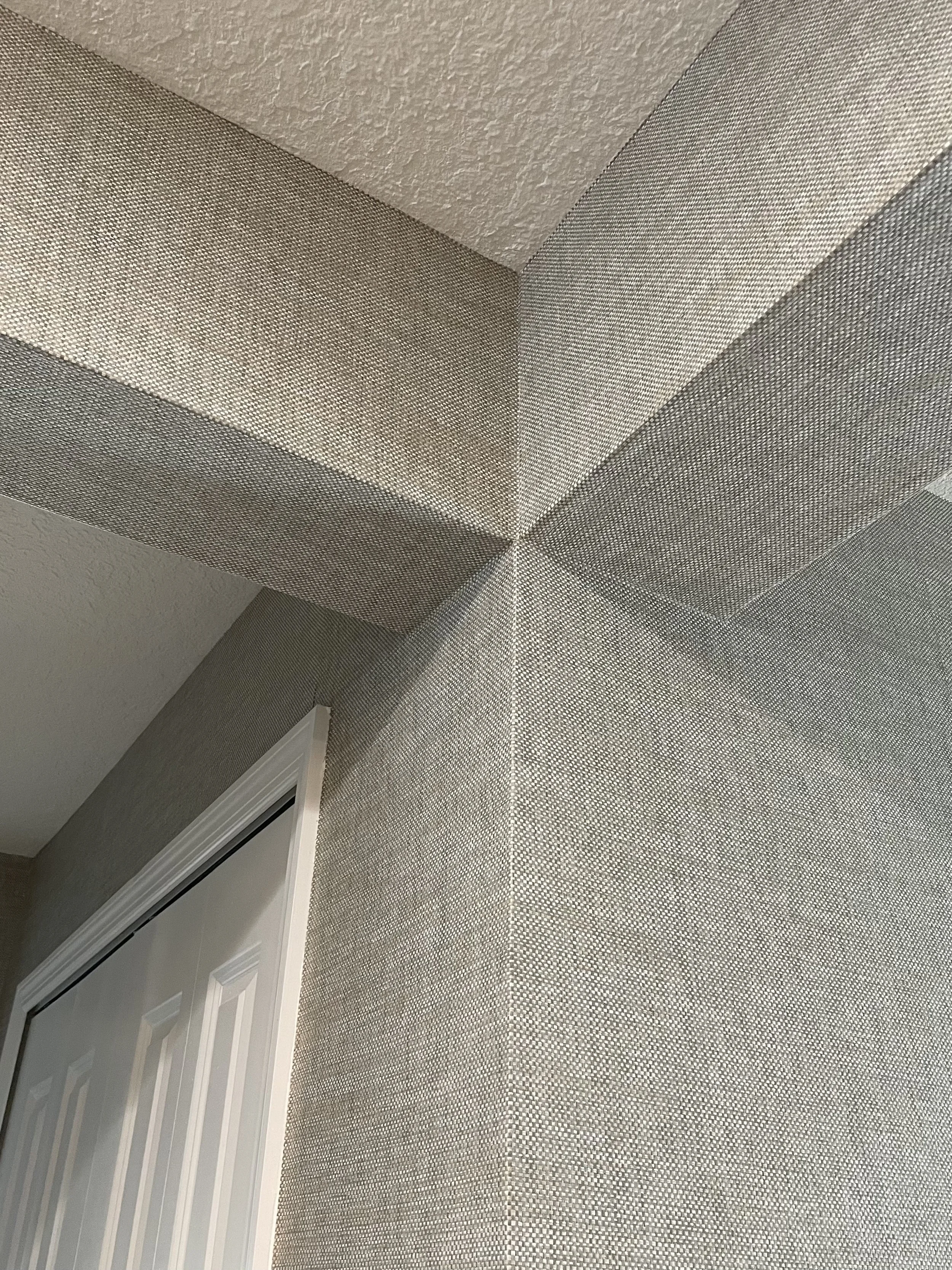 Close-up of gray textured geometric wallpaper on an interior wall and ceiling corner above a doorway.