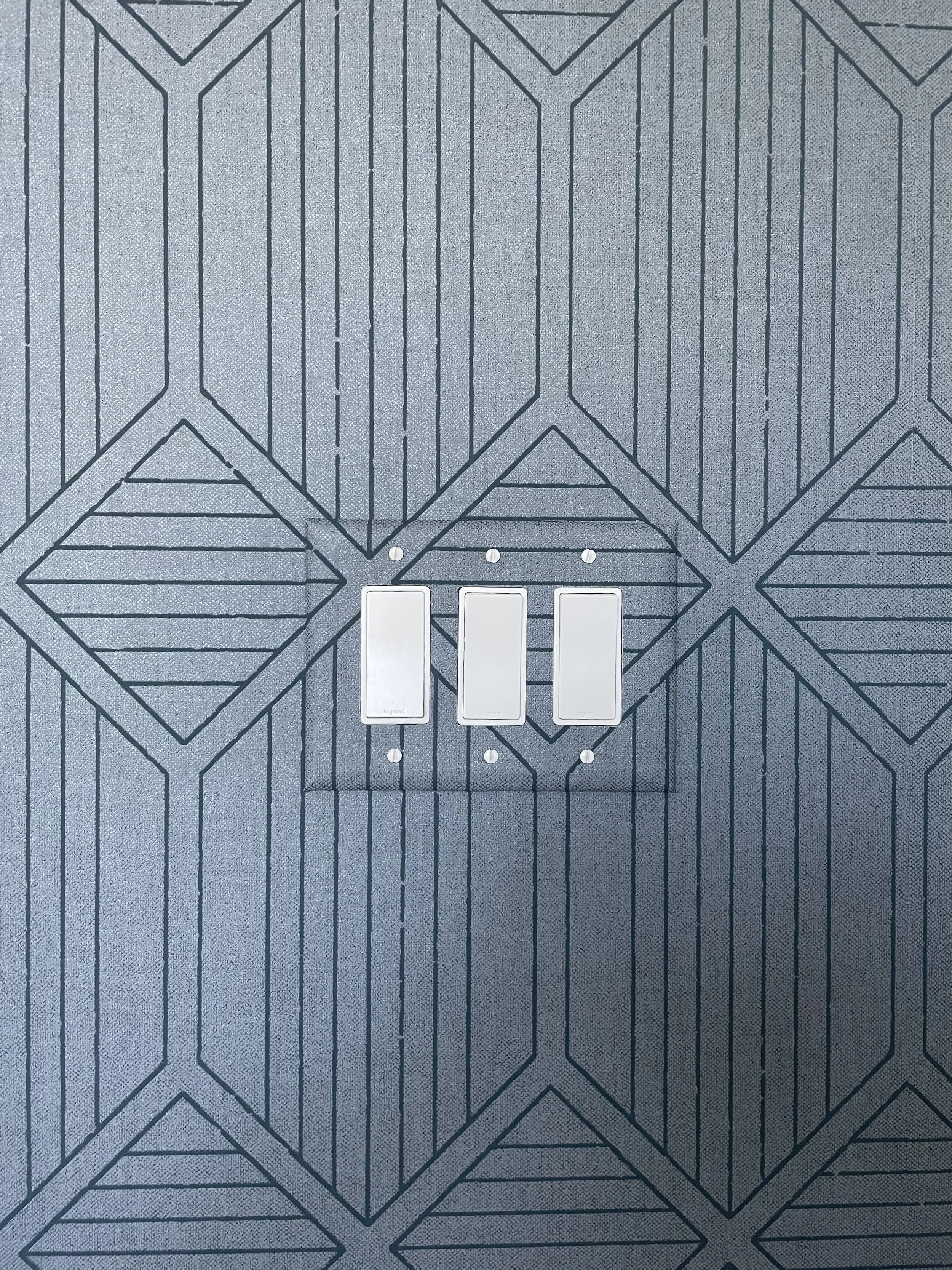 Three white wall light switches mounted on blue-gray geometric patterned wallpaper.