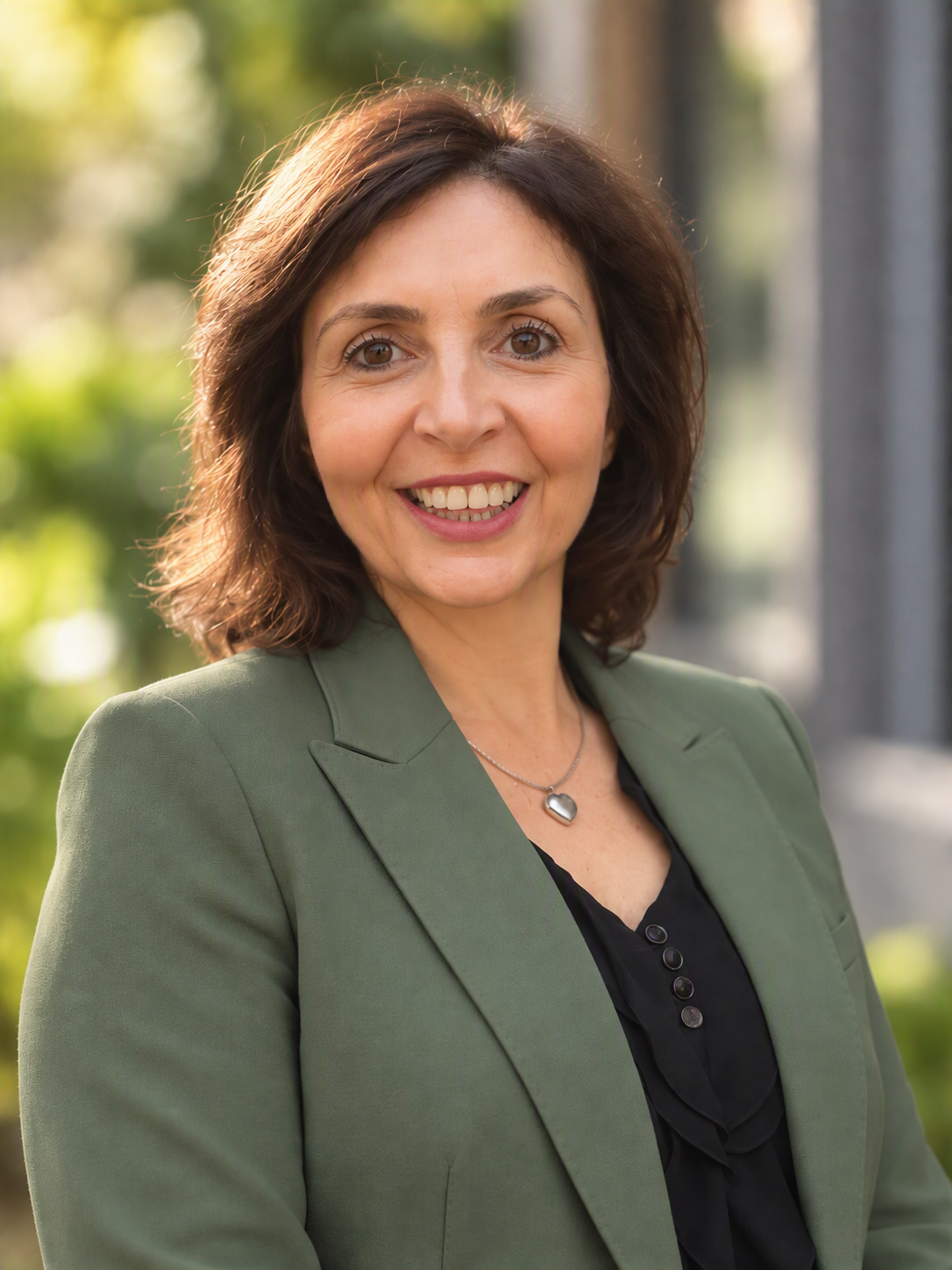 Smiling professional woman in a green blazer and heart necklace posing outdoors