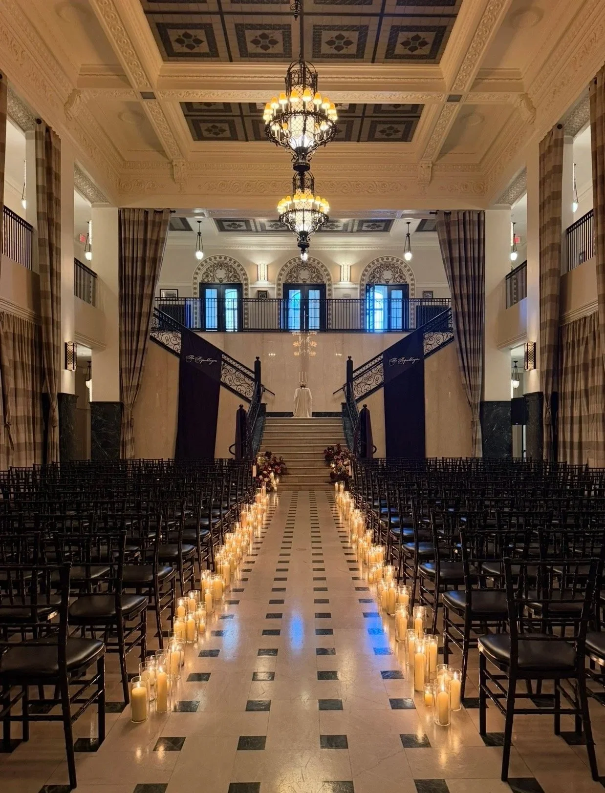 Elegant indoor wedding venue with a grand staircase at the altar, rows of chairs, and candles lining the aisle.