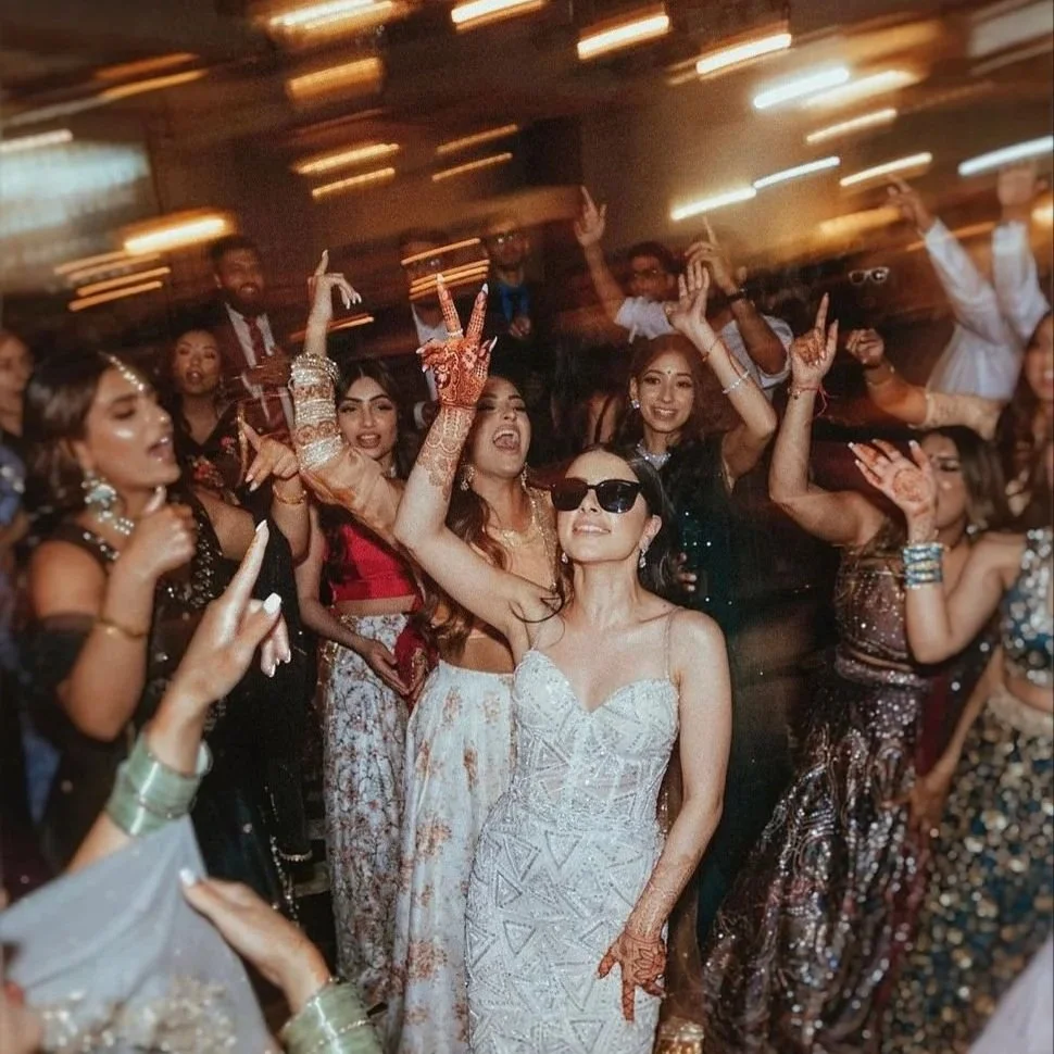Bride in a silver embellished dress celebrates with friends dancing at a lively wedding reception.
