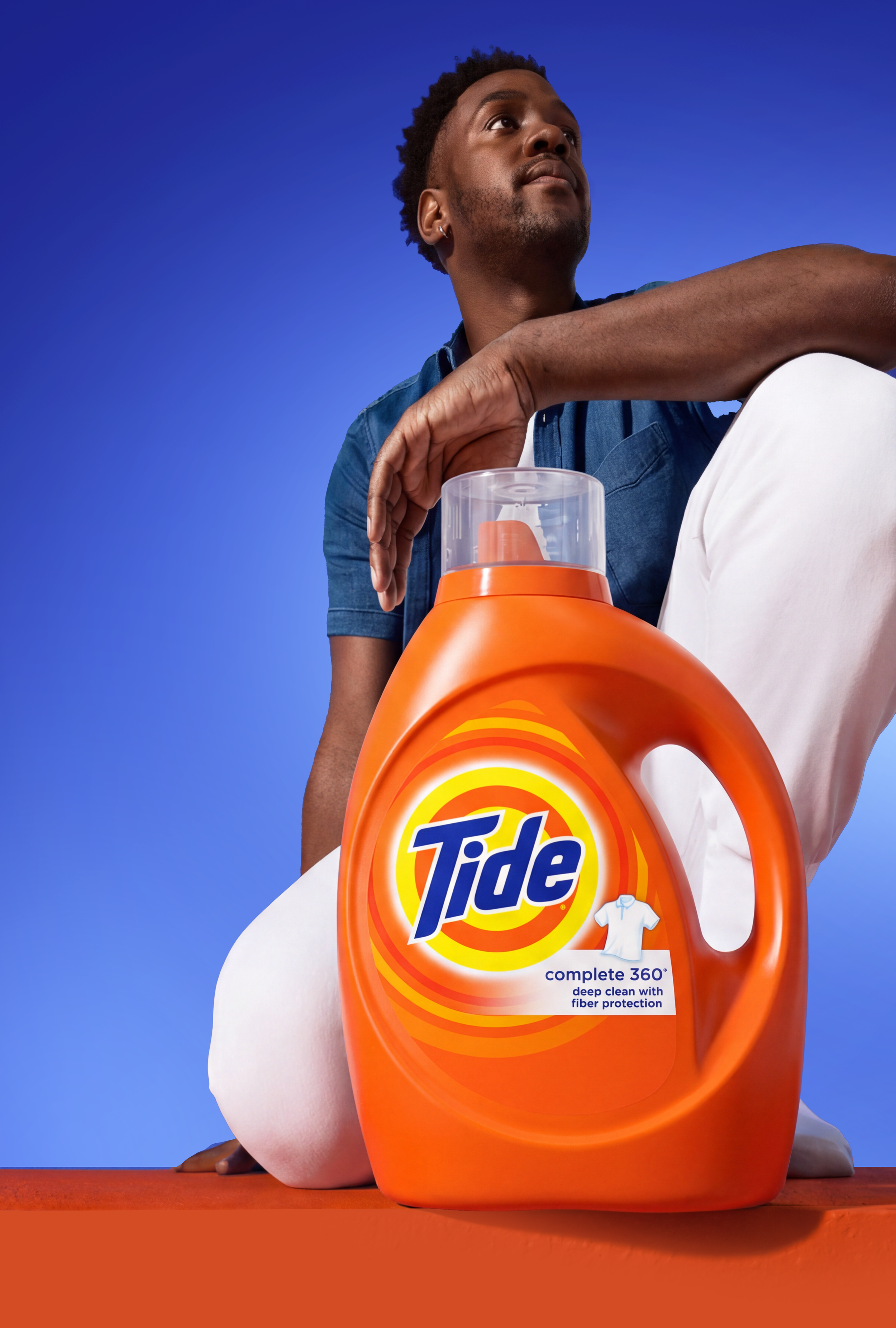 Man holding a large orange Tide laundry detergent jug against a blue background