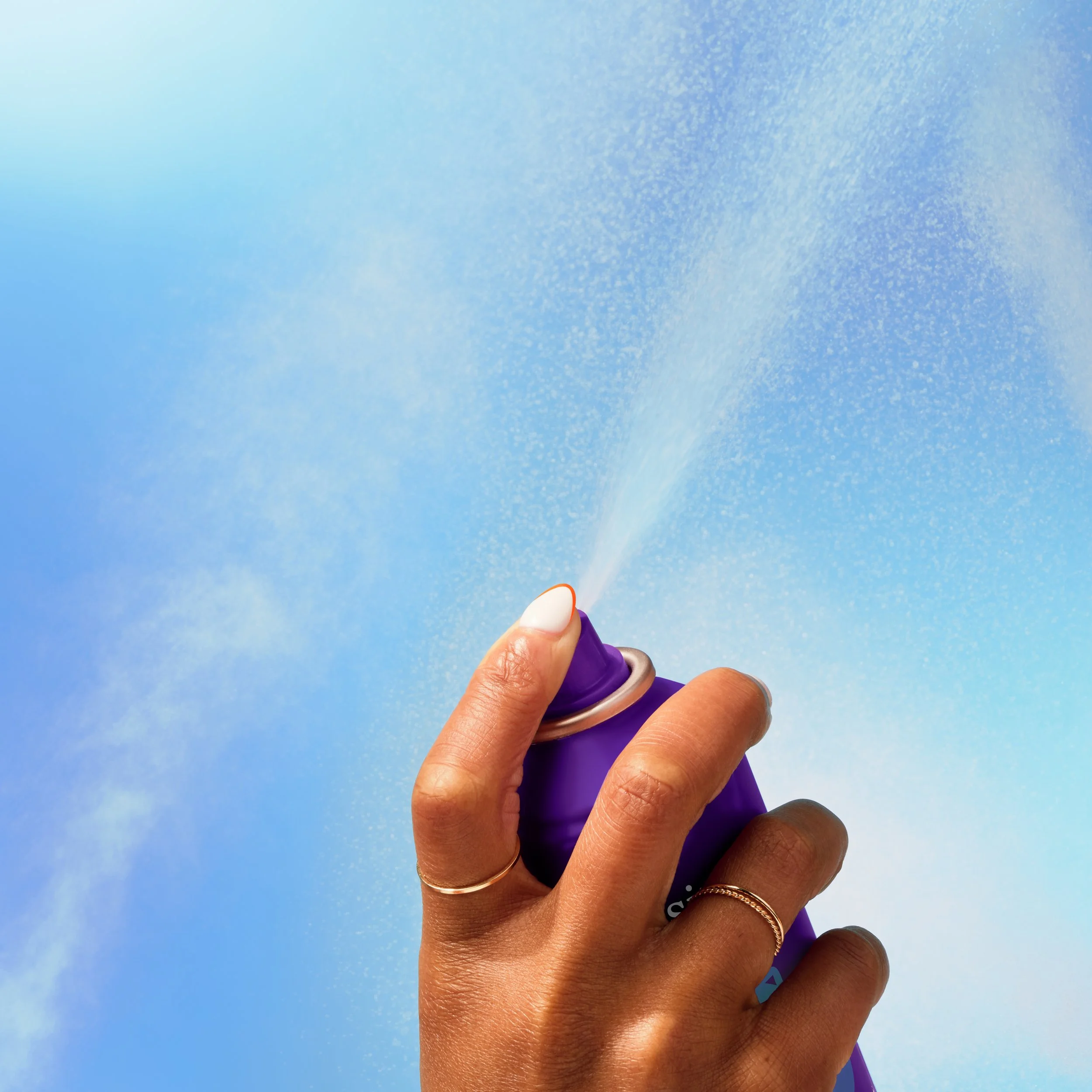 Hand pressing the nozzle of a purple aerosol spray can against a blue background