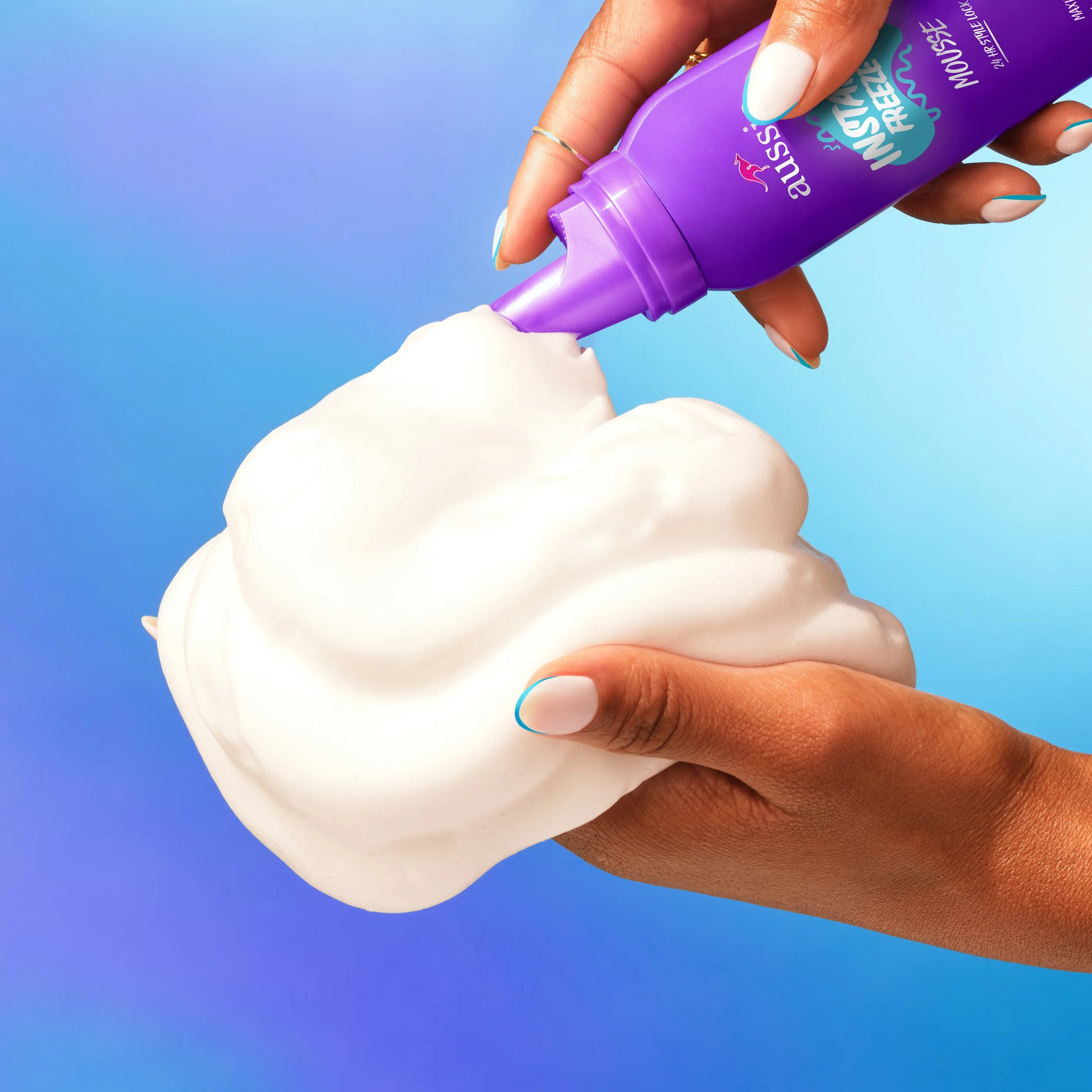 Hand dispensing white shaving cream from a purple tube onto a mound of whipped foam.