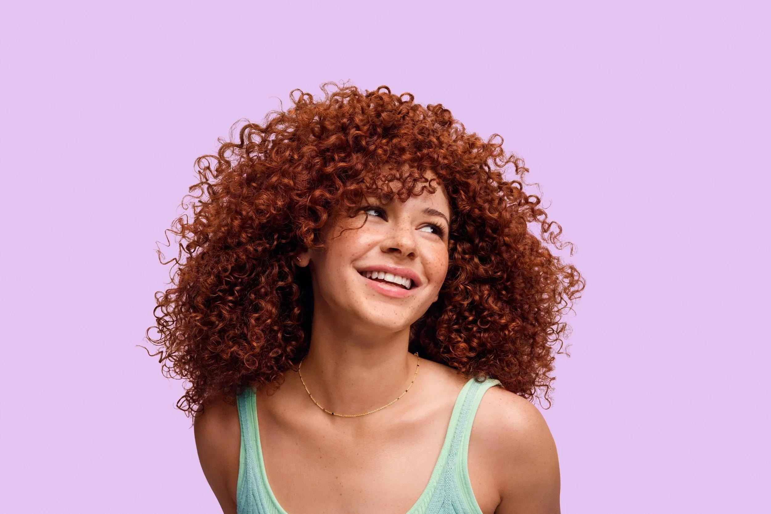 Smiling woman with voluminous curly auburn hair against a lavender background
