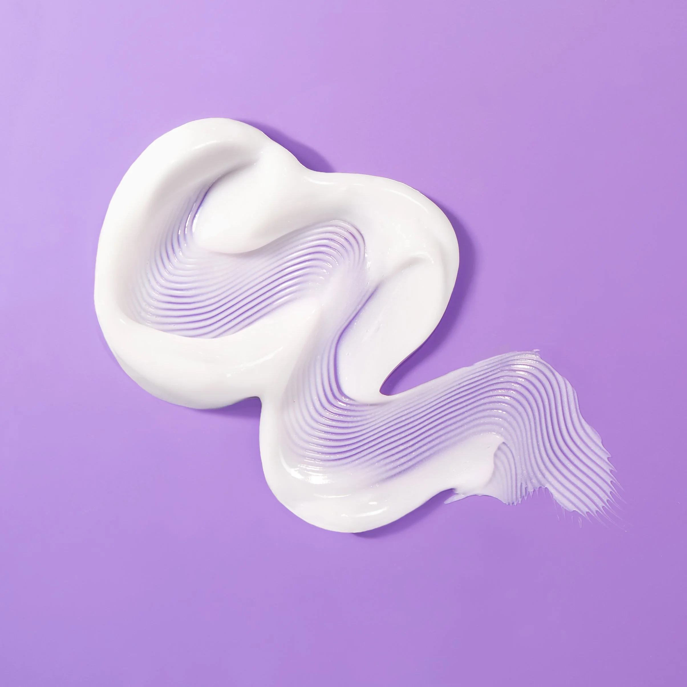 White cream squeezed in a flowing ribbon pattern on a purple background