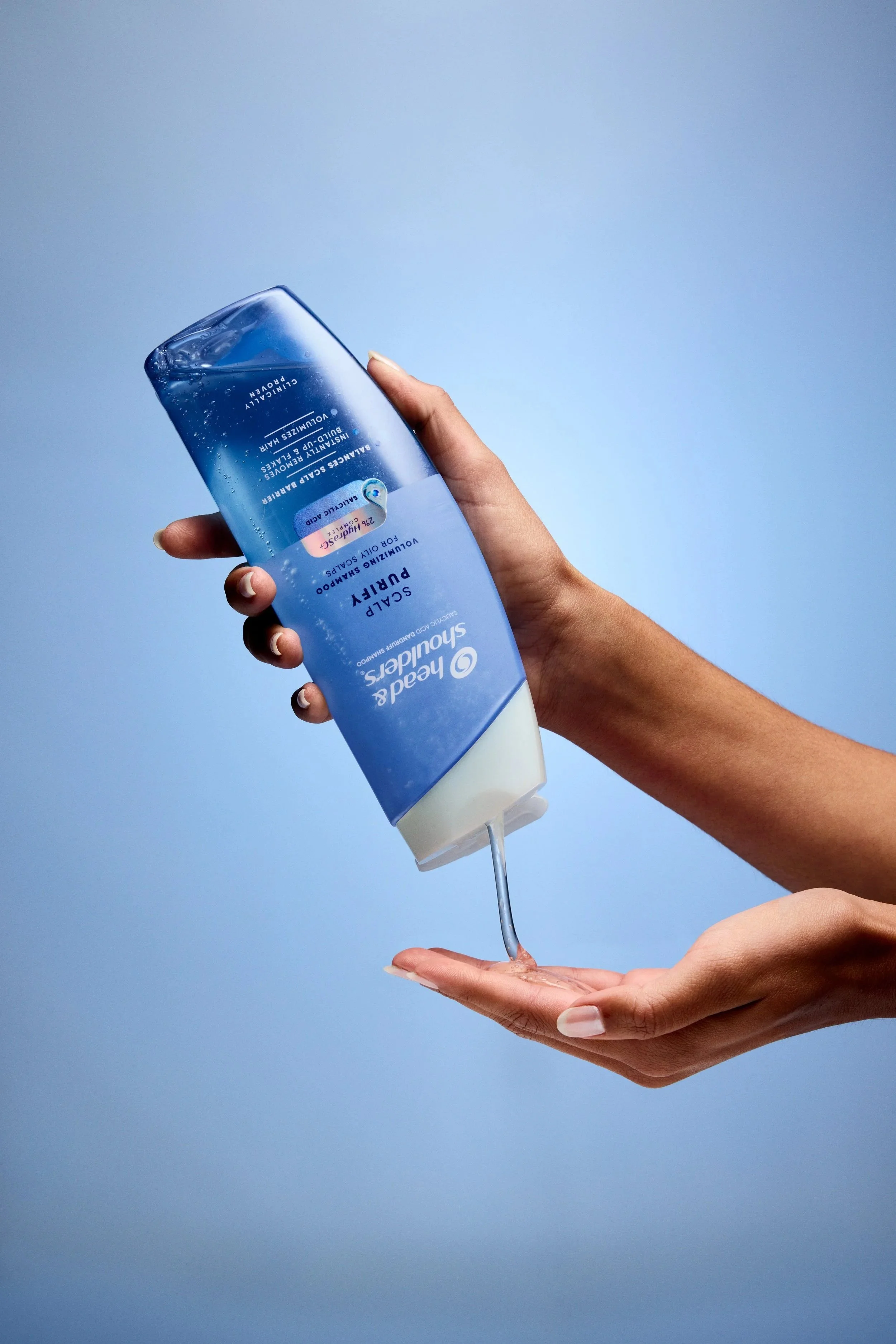 Person pouring Head & Shoulders Classic Clean shampoo into an open hand against a blue background
