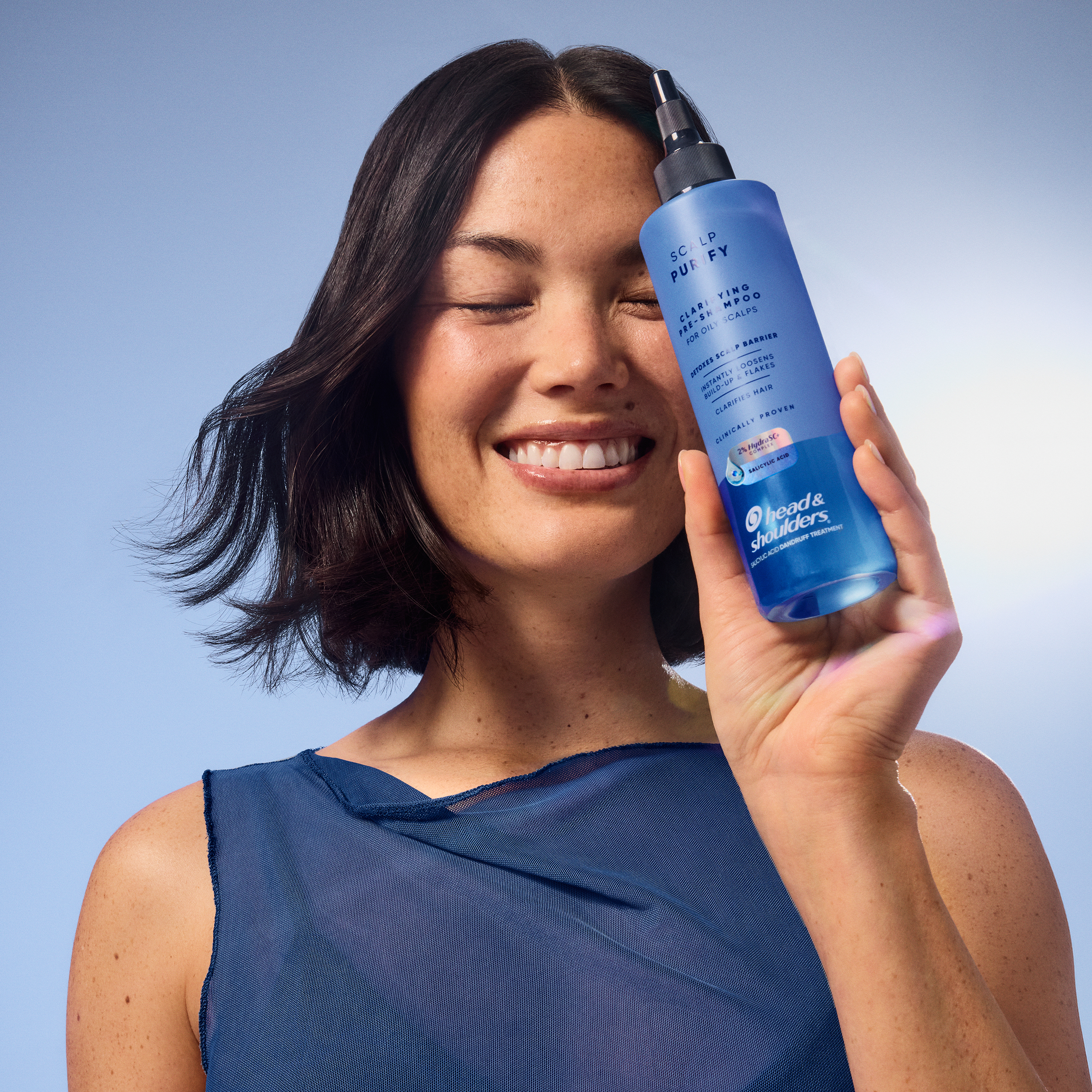 Smiling woman holding a blue Head & Shoulders Scalp Purify shampoo bottle