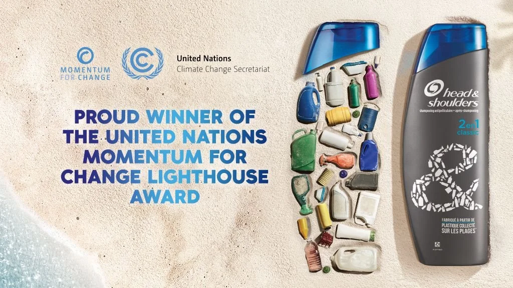 Head & Shoulders 2-in-1 shampoo bottle beside ocean plastic waste on a beach, with United Nations Momentum for Change Lighthouse Award text