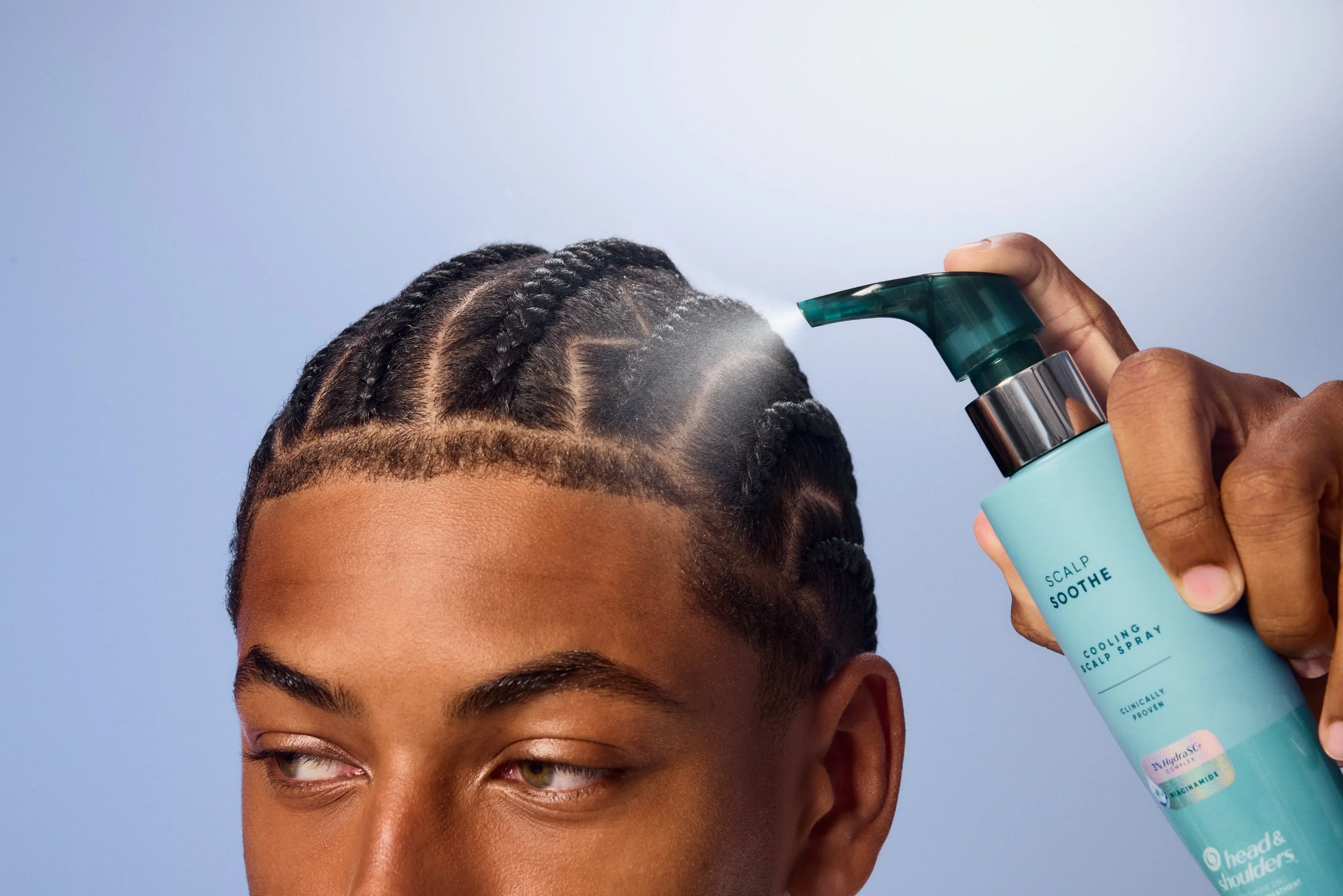 Person with braided hair spraying Head & Shoulders Scalp Soother cooling scalp spray on their scalp