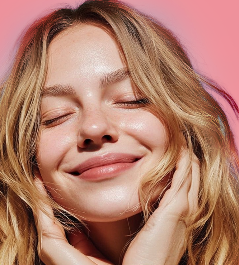 Close-up portrait of a smiling blonde woman with closed eyes against a pink background