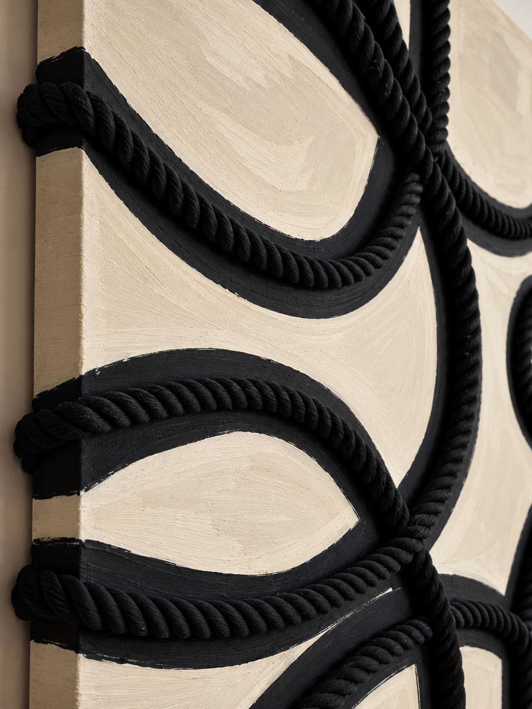 Close-up of black braided rope arranged in geometric patterns on a textured cream and black wall panel