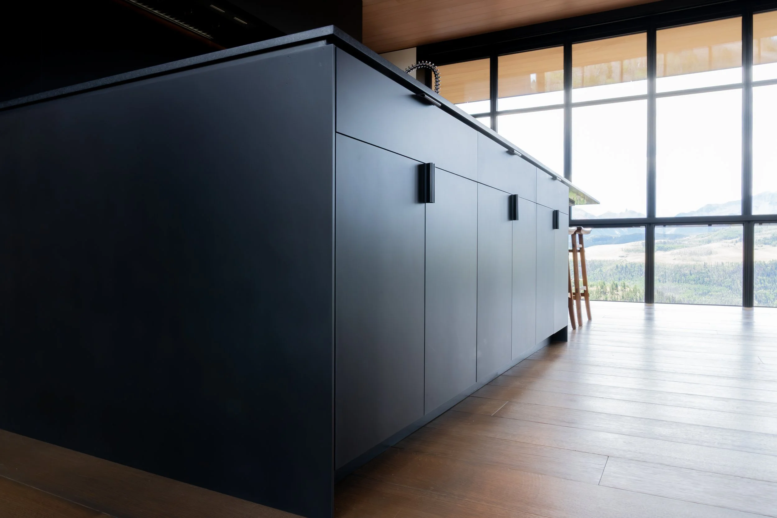 Modern kitchen with black cabinets and large windows overlooking a mountainous landscape.