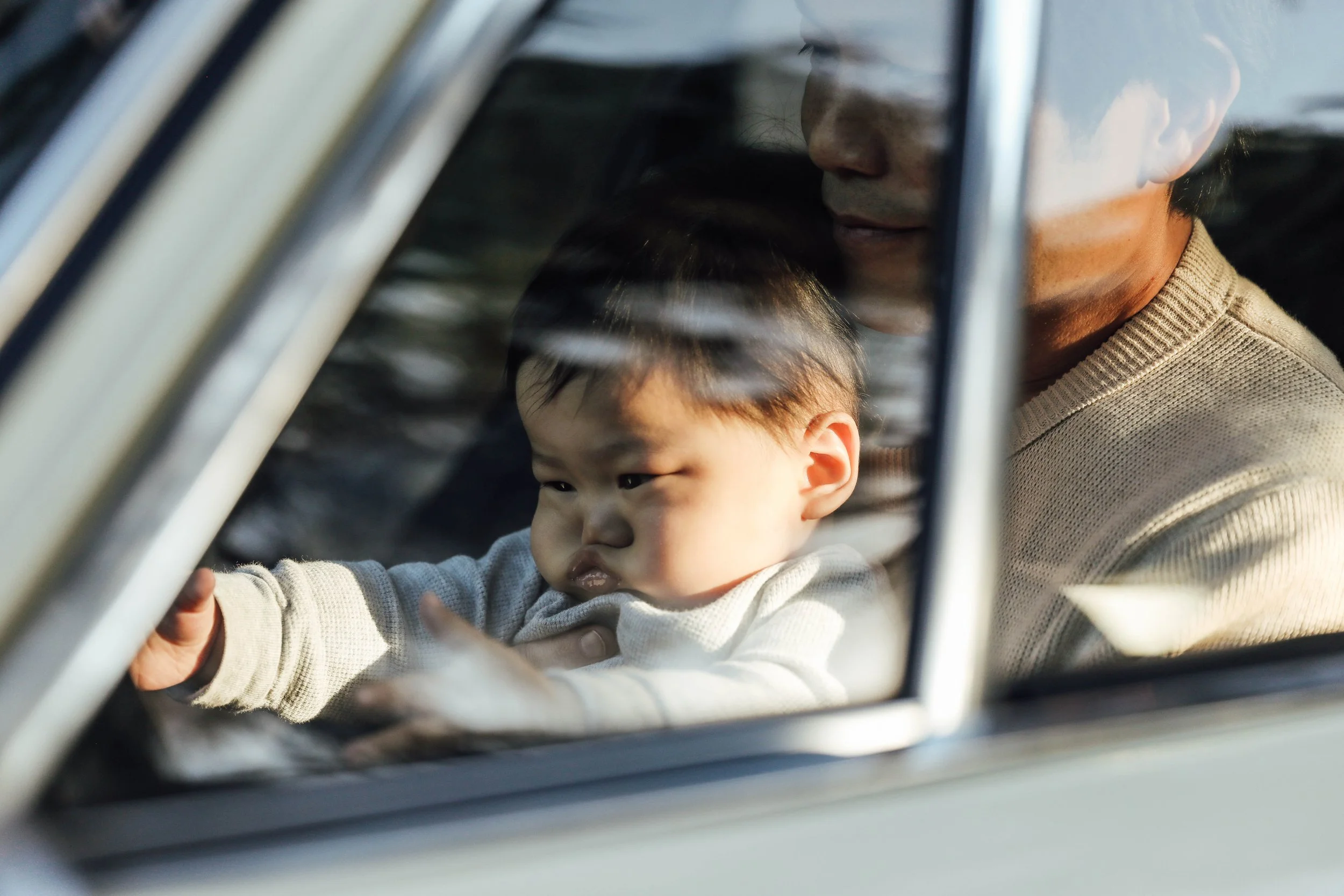 A young boy looking out the window of a car while an adult, possibly his father, is visible nearby inside the vehicle.