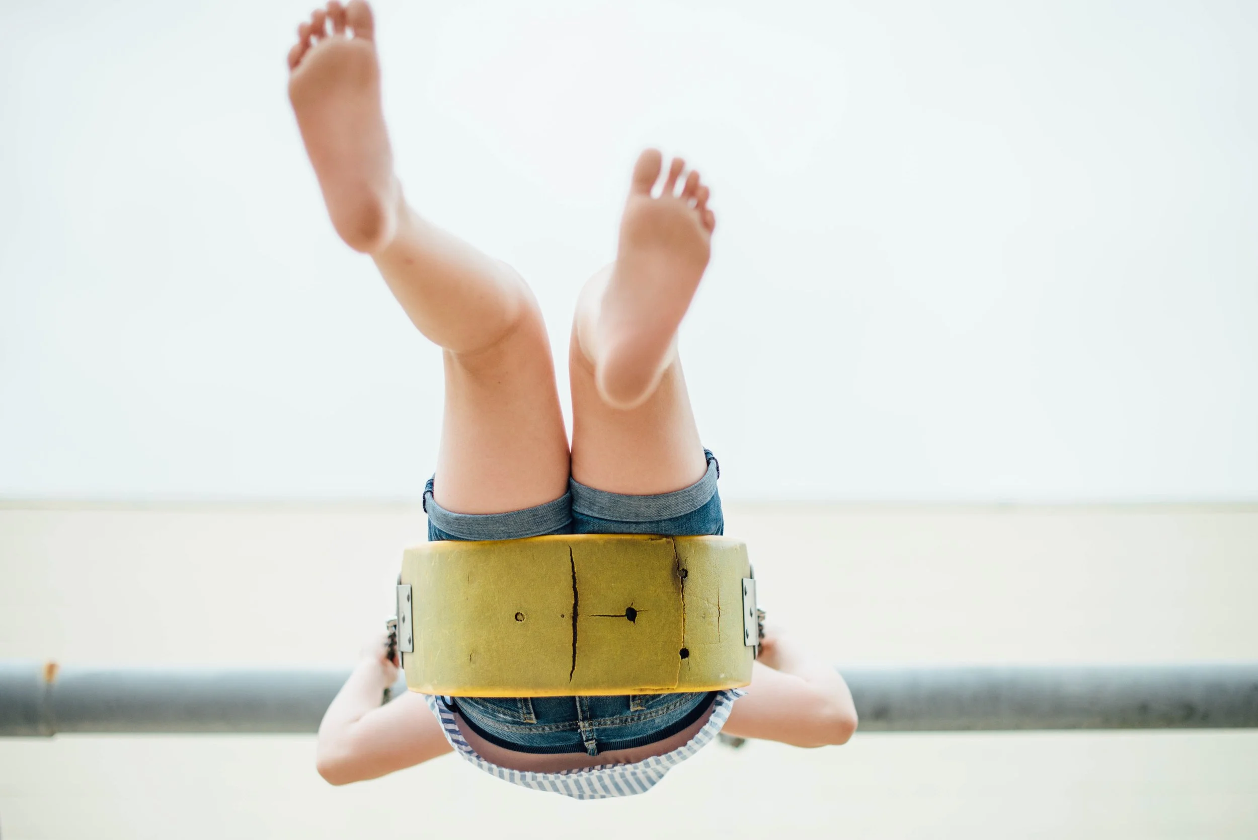 Child standing inside a wooden barrel, with legs raised and feet visible, against a plain white background.
