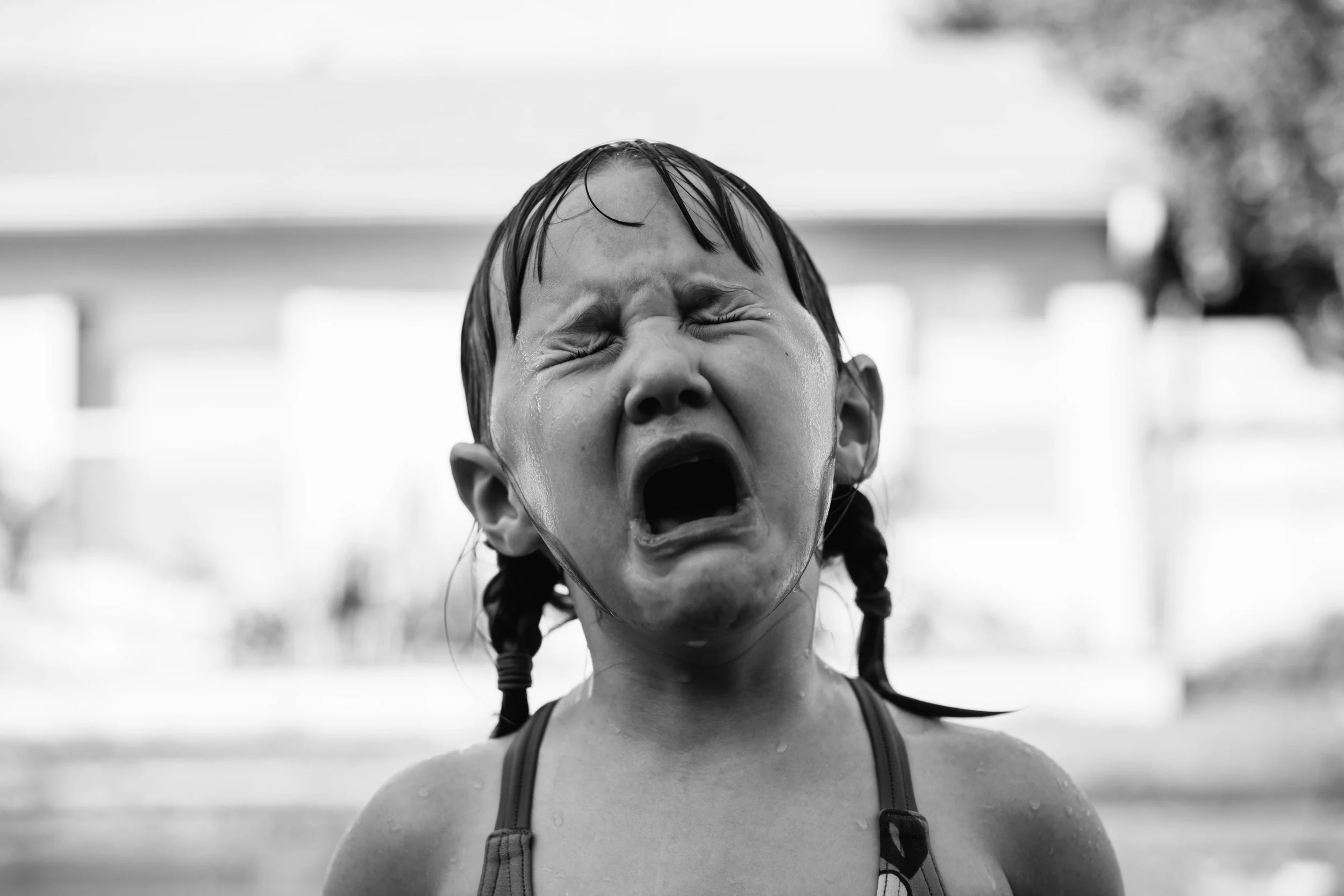 A young girl with wet hair and tears on her face, crying with her mouth open, outside on a cloudy day.