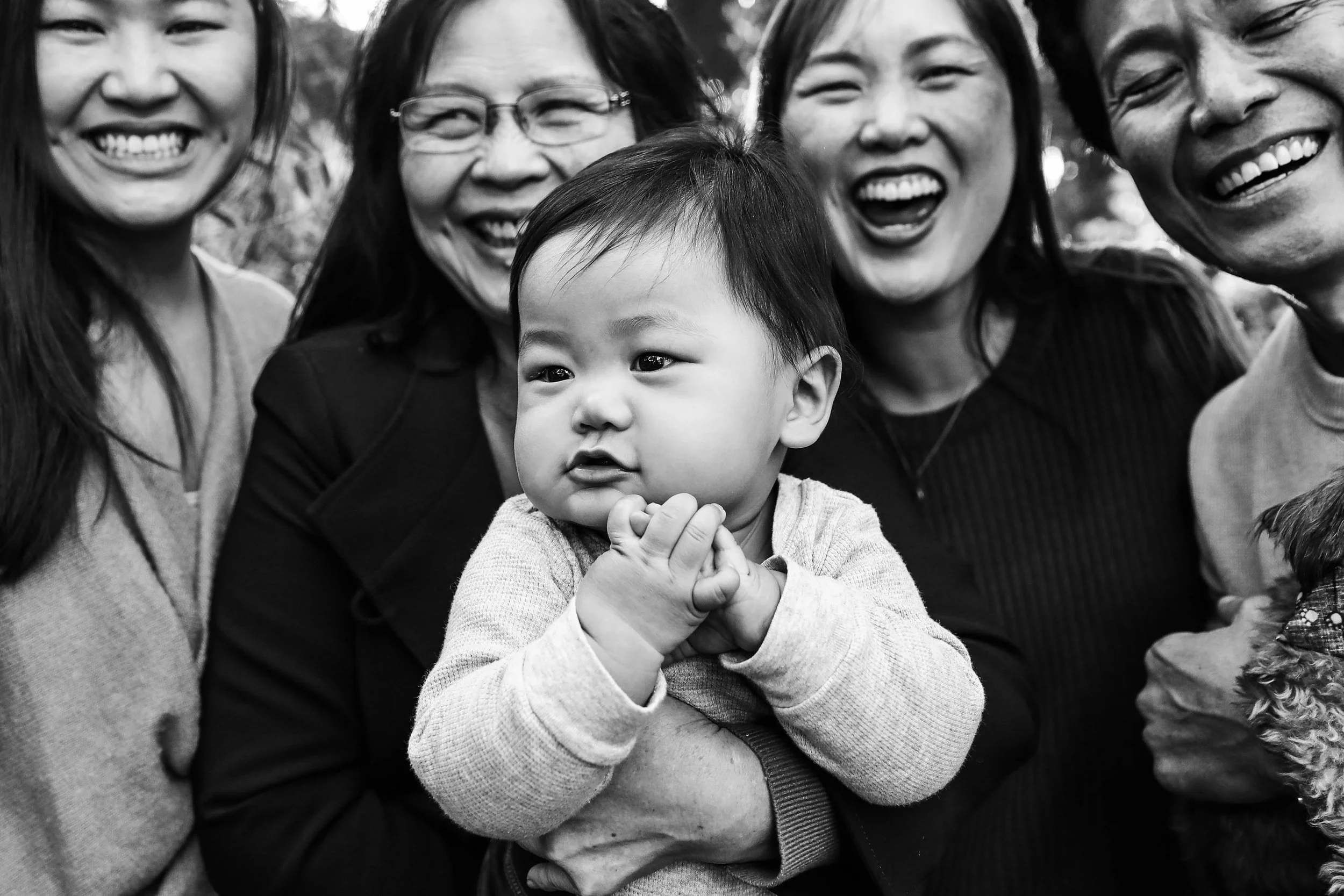 Black and white photo of a group of smiling women and a young child, posing closely together outdoors.