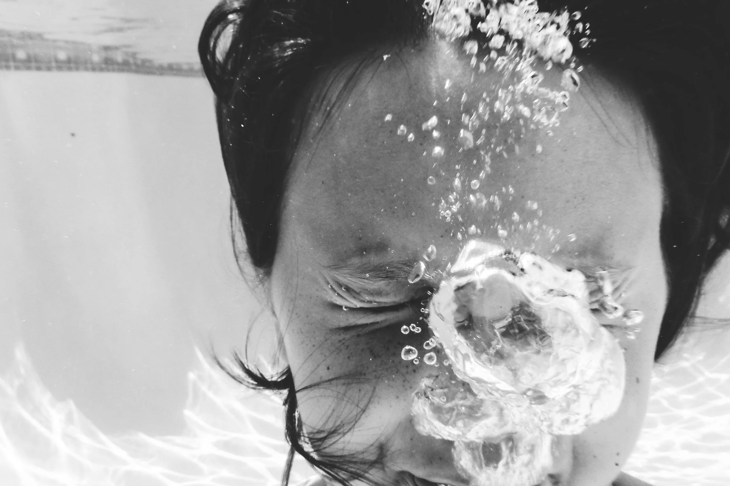A person submerged underwater, with only part of their face and hair visible, surrounded by bubbles.