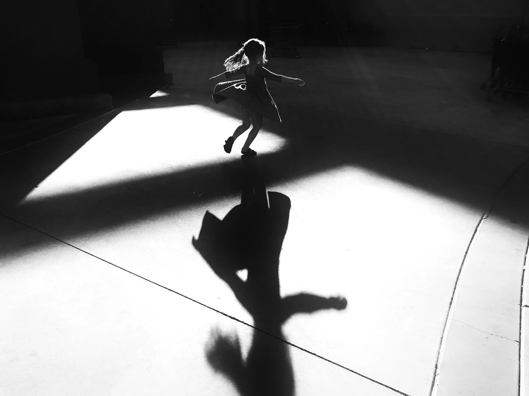 A girl twirling in a dark space with bright light creating a shadow on the floor.