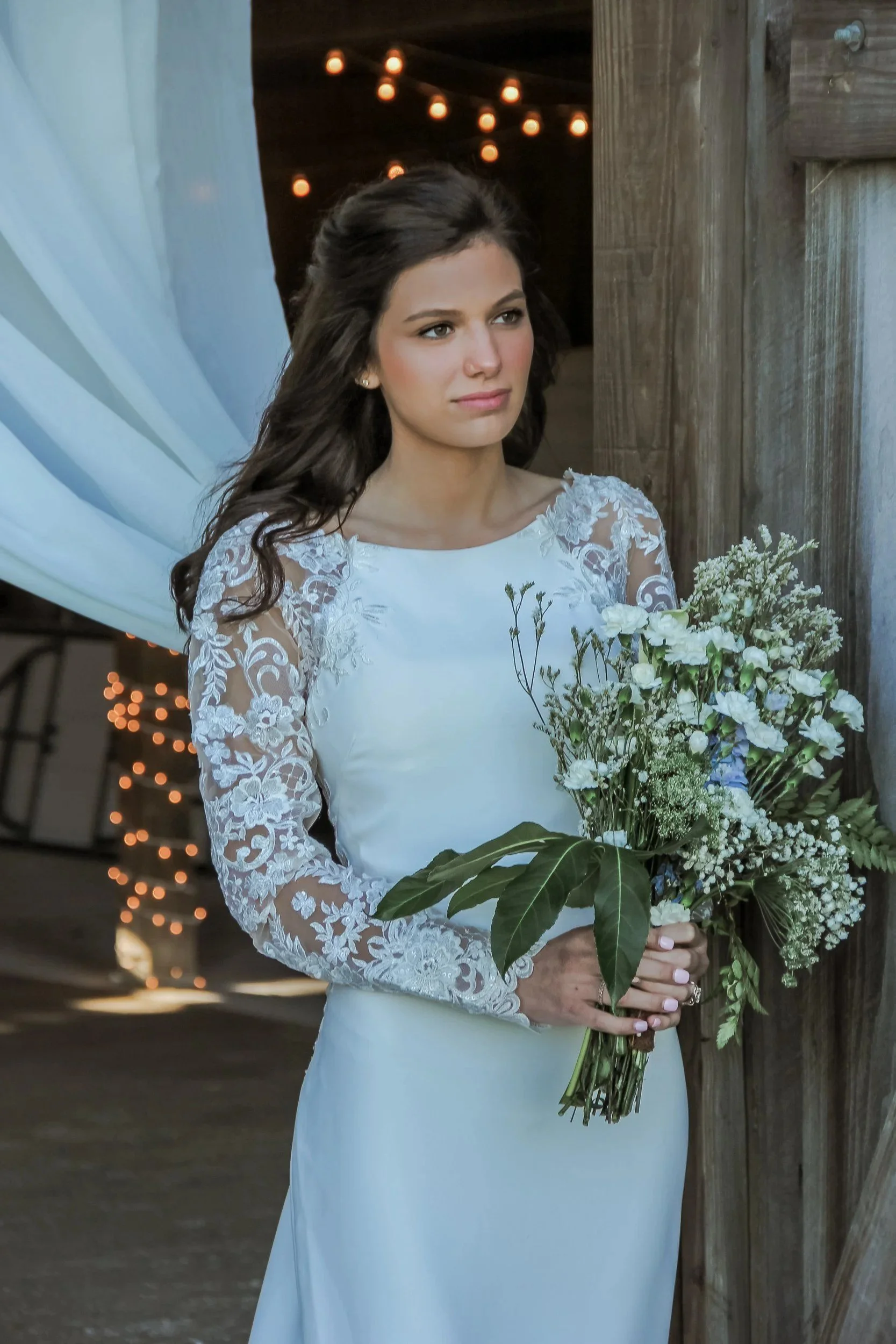 Bride in a long-sleeve lace dress holding a baby's breath bouquet