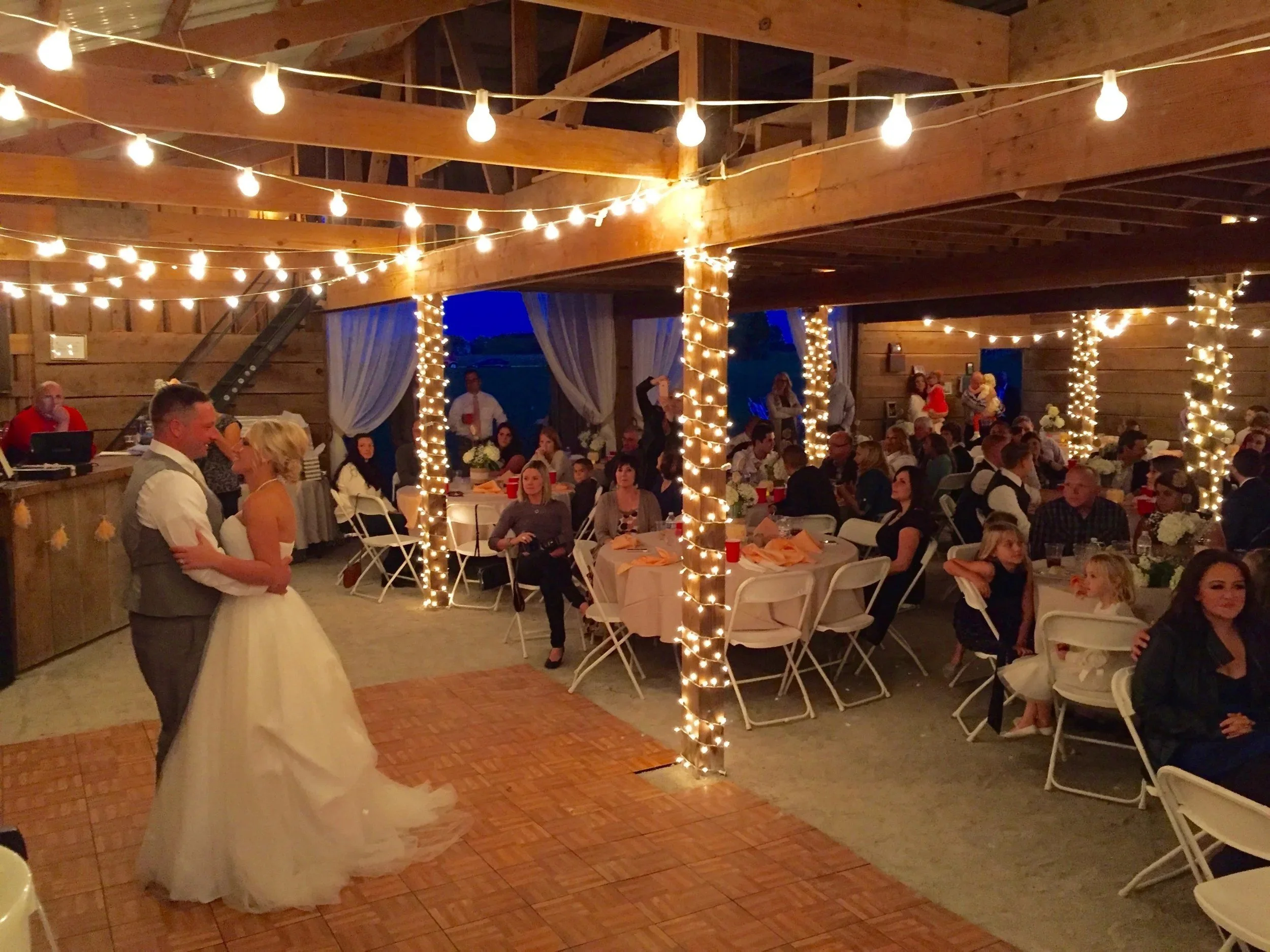 Reception tables under string-light posts inside the barn