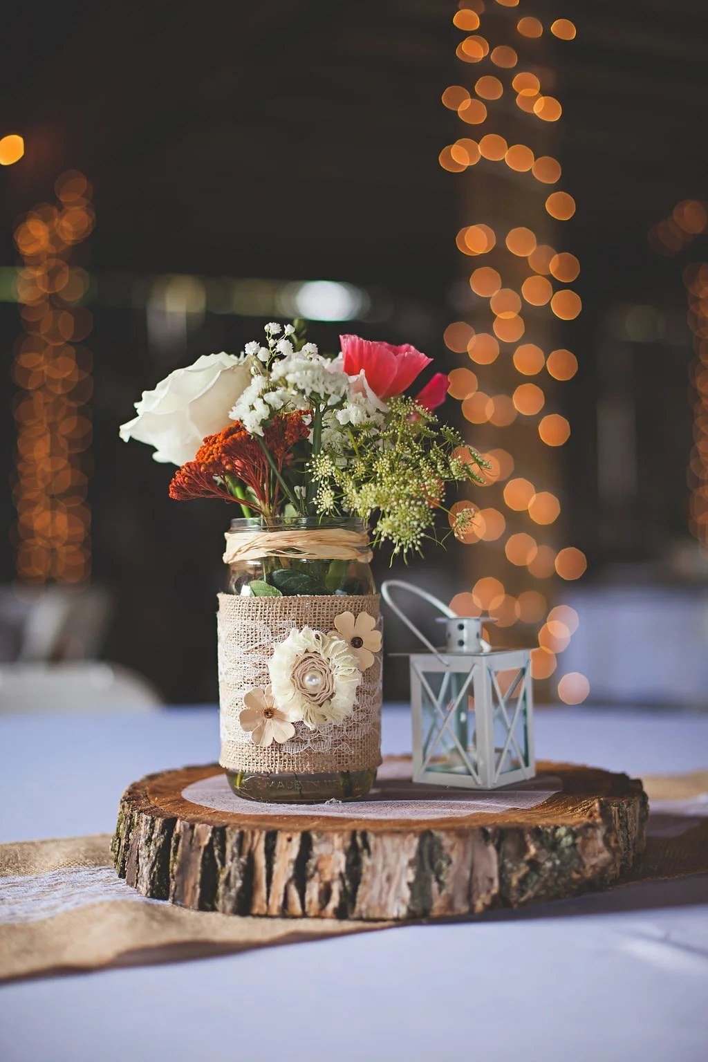 Rustic centerpiece with flowers in a lace-wrapped mason jar on a wood slice