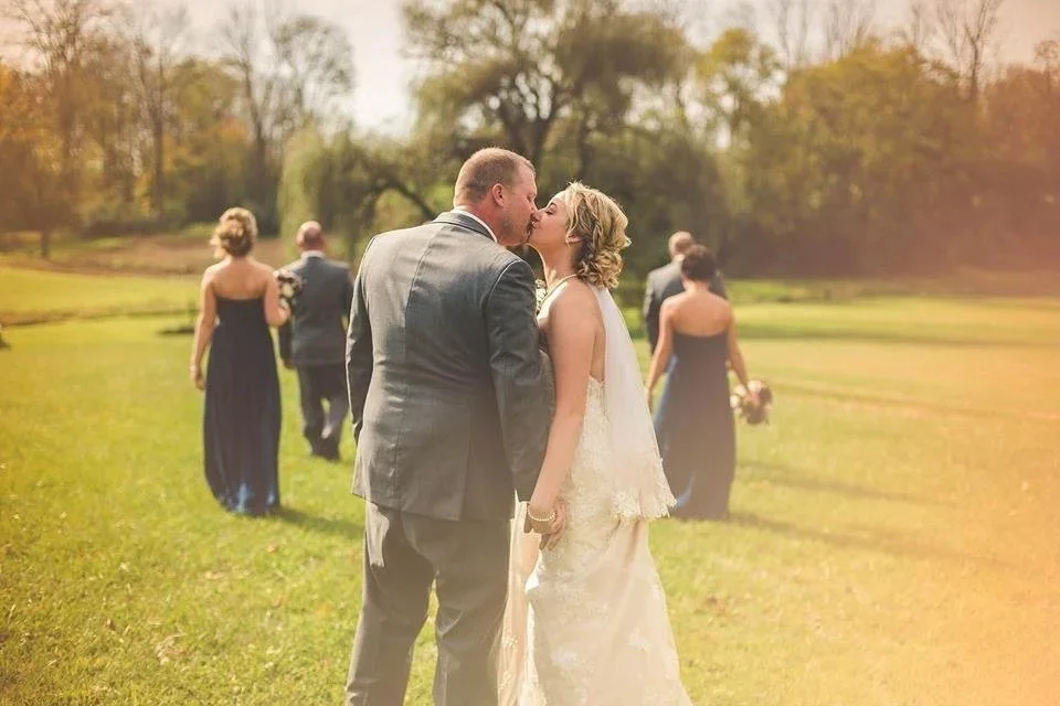 Couple kissing on the lawn with the wedding party behind them