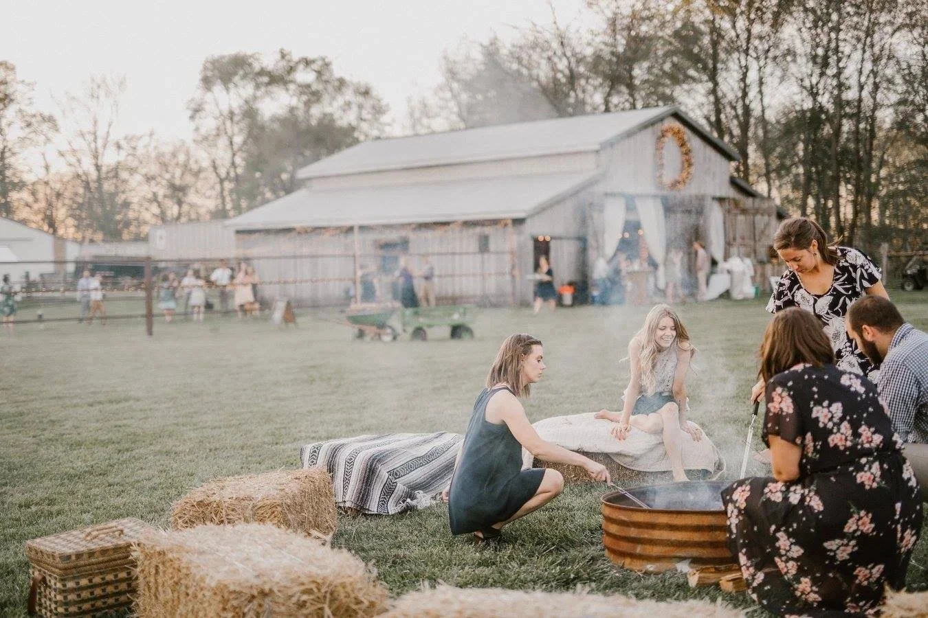 Guests relaxing by a fire pit with hay bales near the barn