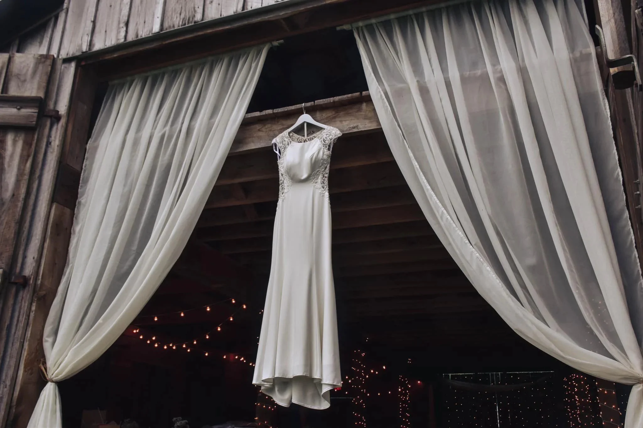 Wedding dress hanging between white drapes in the barn doorway