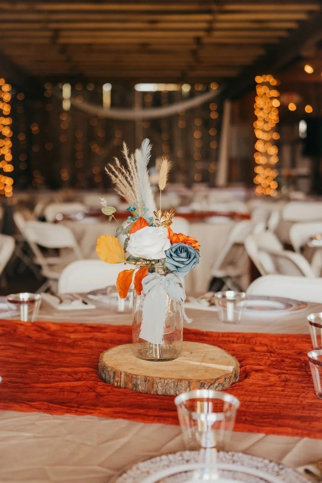Orange and blue floral centerpiece on a reception table inside the barn