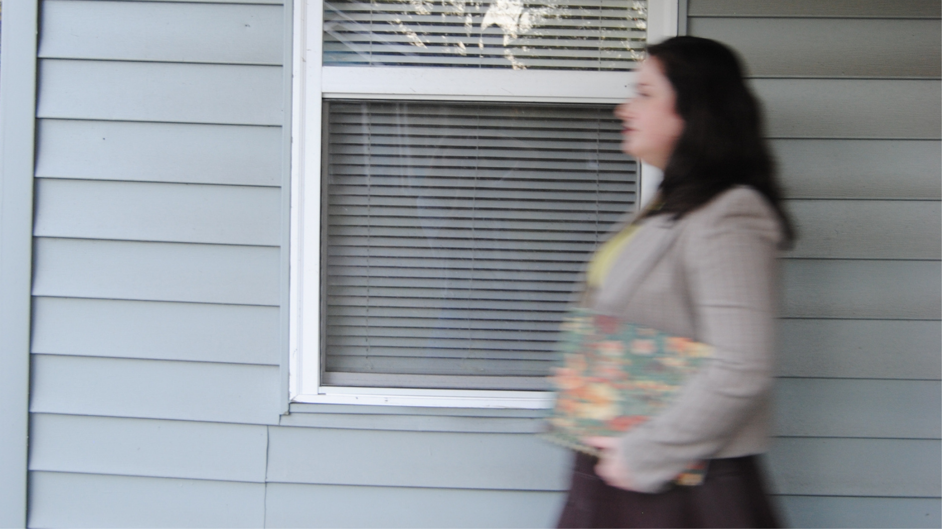 Woman walking past a house window while carrying a colorful patterned shoulder bag