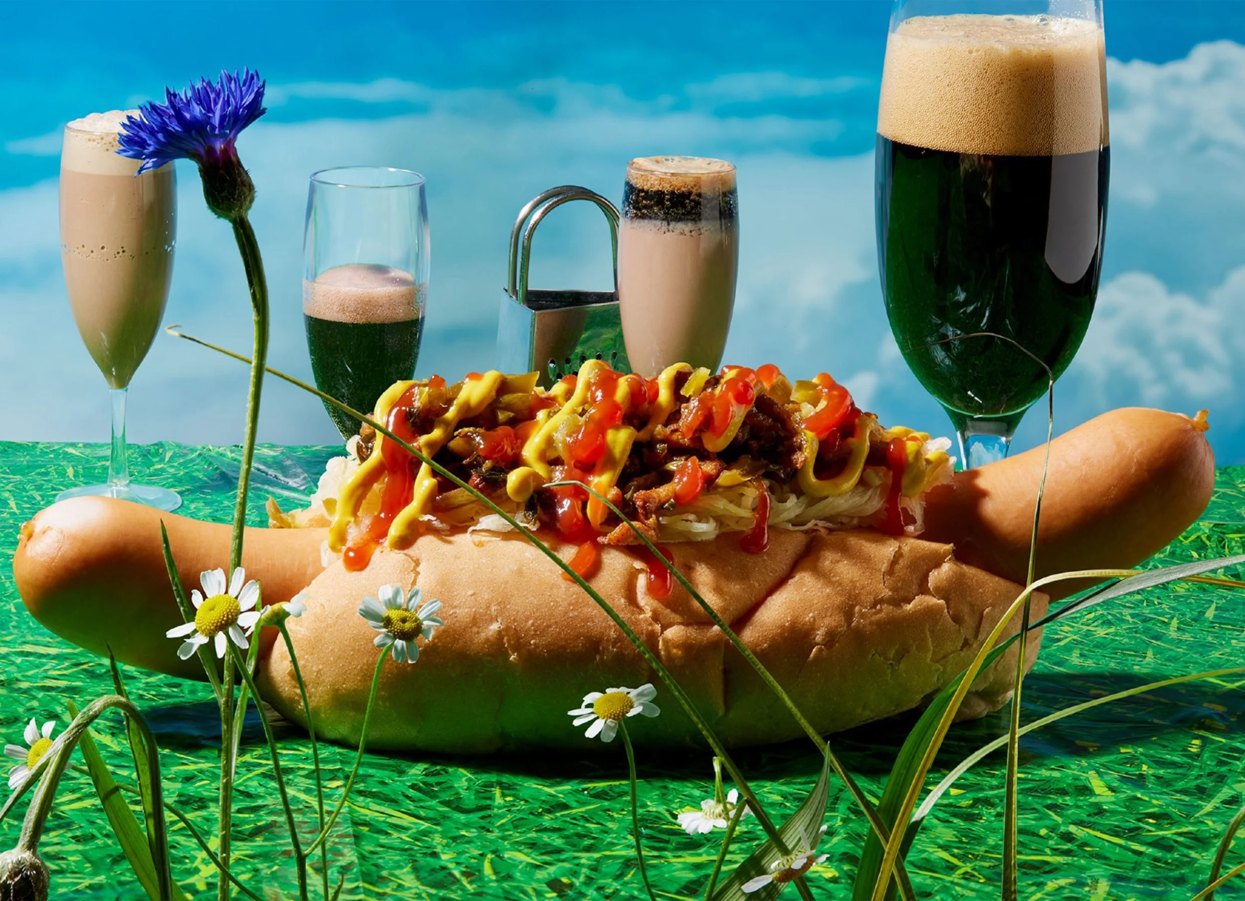 Loaded hot dog with mustard and ketchup, surrounded by beer glasses, flowers, and a blue sky background