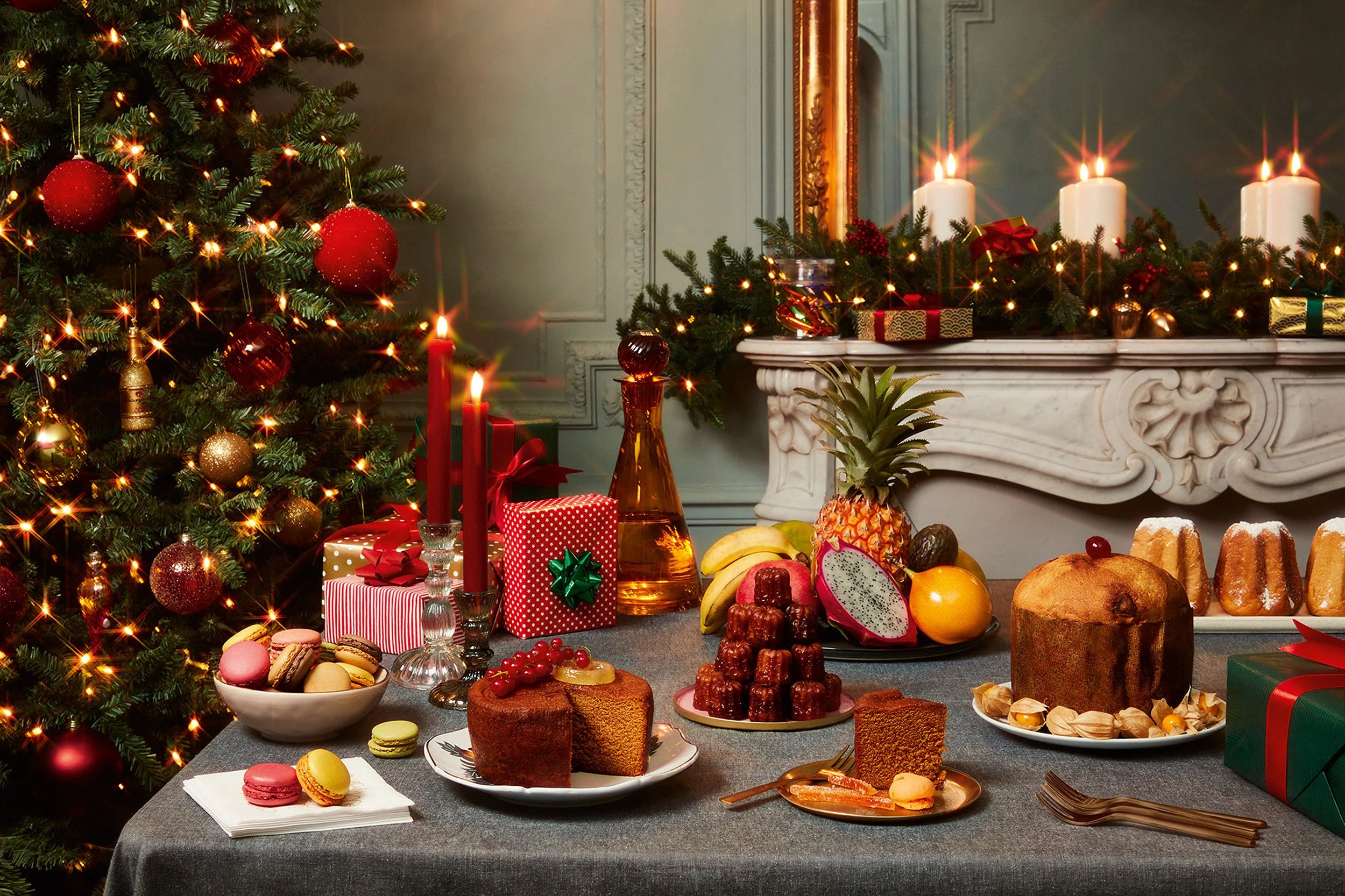 Festive Christmas dining table with decorated tree, candles, gifts, fruit, pastries, and holiday desserts
