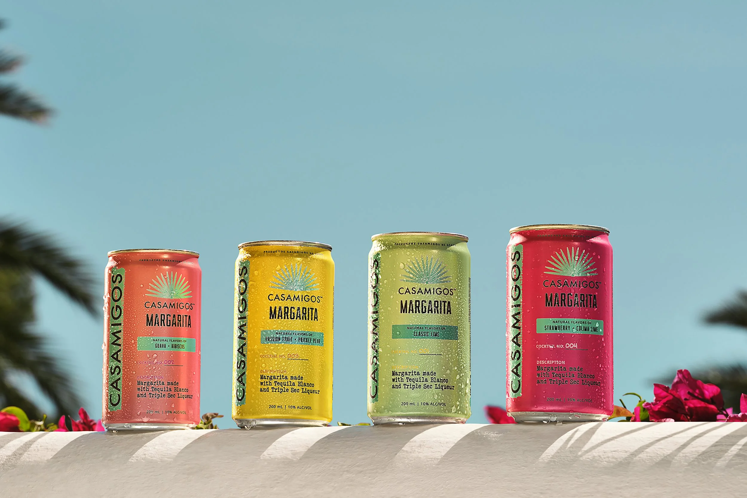 Four colorful Casamigos Margarita cans in guava hibiscus, passion fruit prickly pear, classic lime, and strawberry lime flavors displayed outdoors.