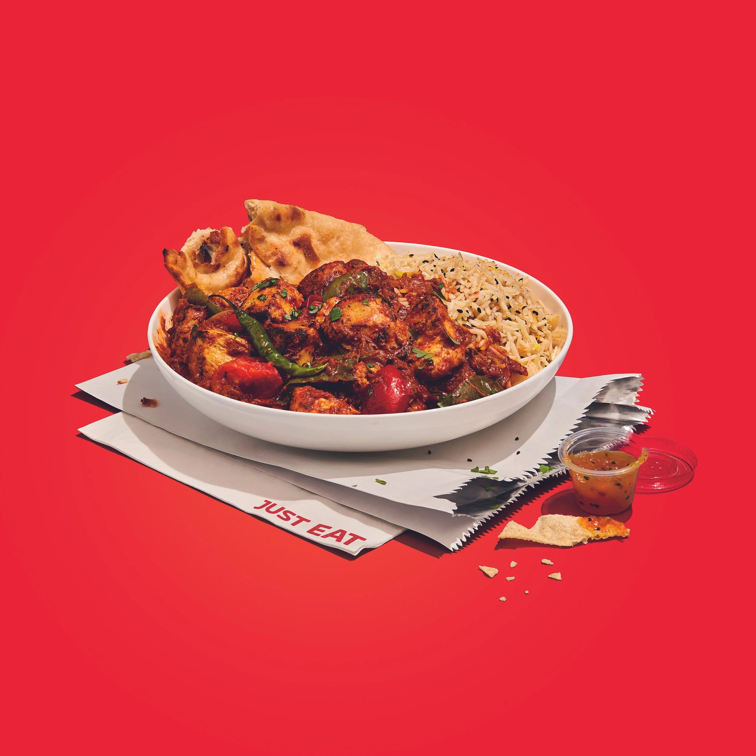 Indian mixed grill platter with grilled chicken, kebabs, basmati rice, naan, and chutney on a red background