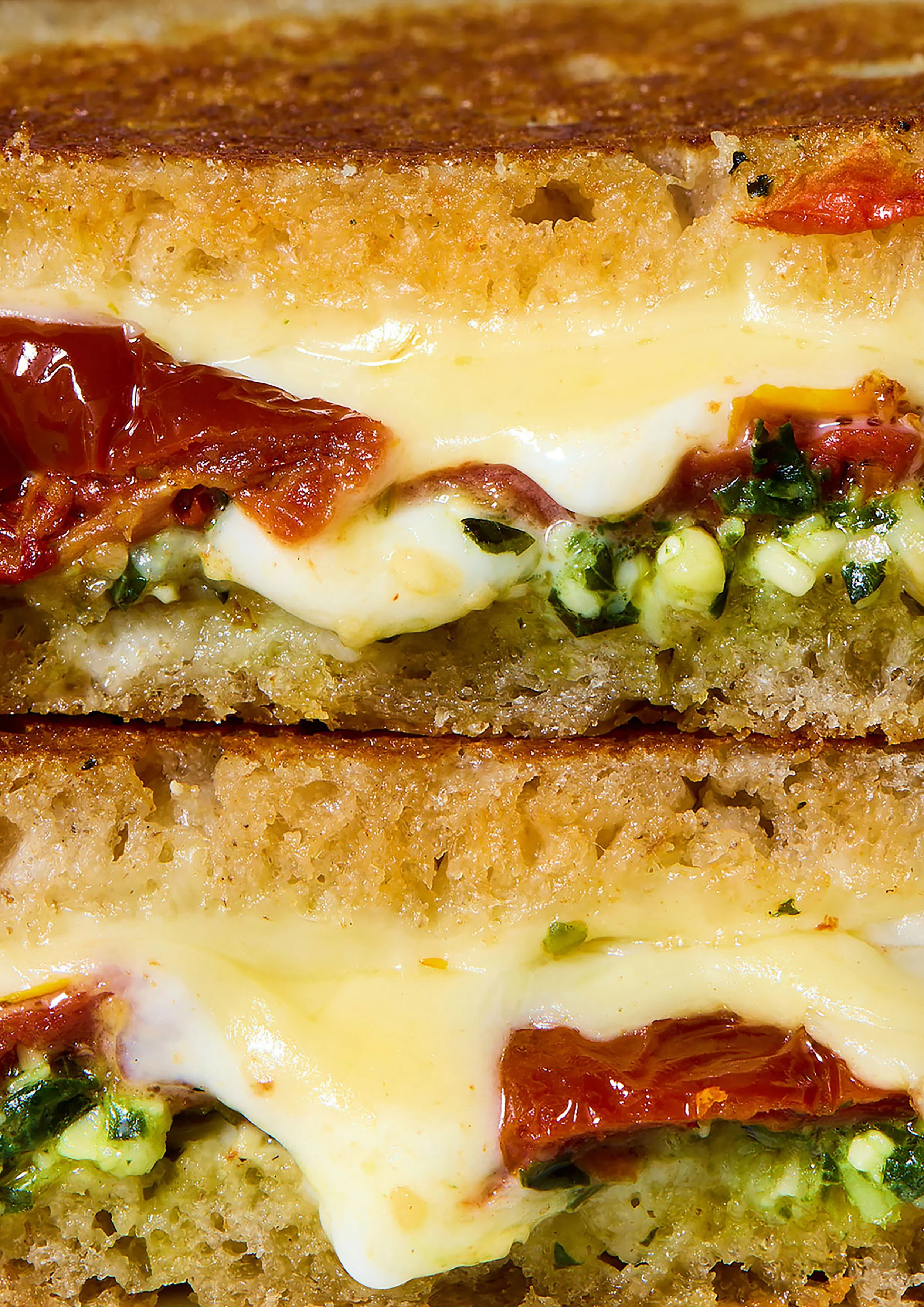 Close-up of a crispy toasted sandwich with melted cheese, tomatoes, herbs, and creamy sauce.