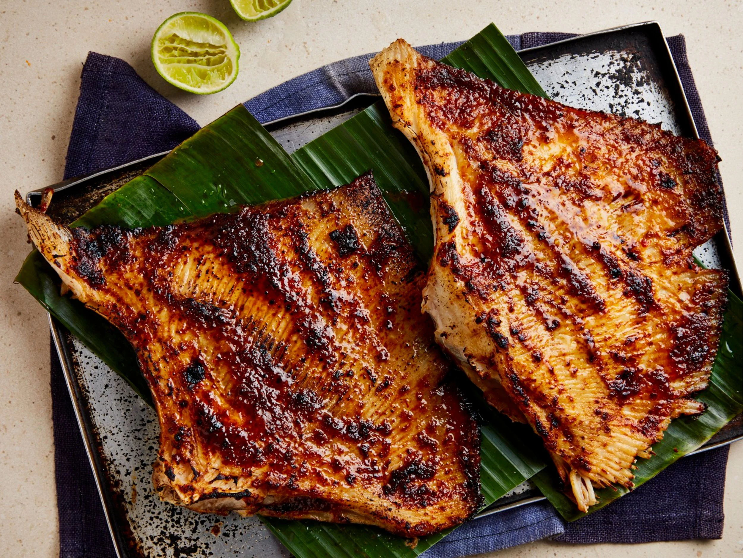 Grilled spicy chicken breasts served on banana leaves with lime halves