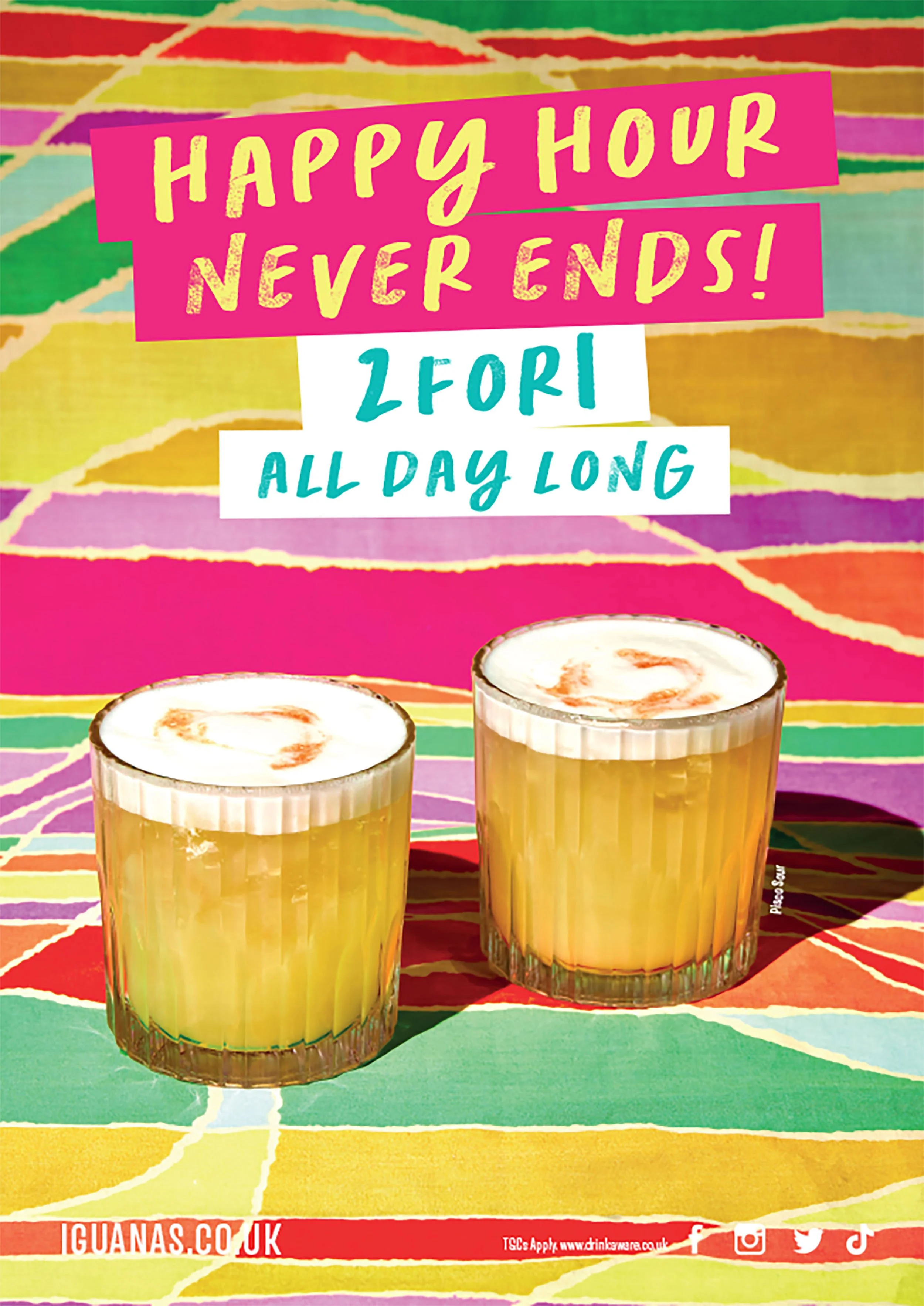Two glasses of yellow cocktails with foamy tops on a colorful patterned table, beneath a sign reading “Happy Hour Never Ends!”